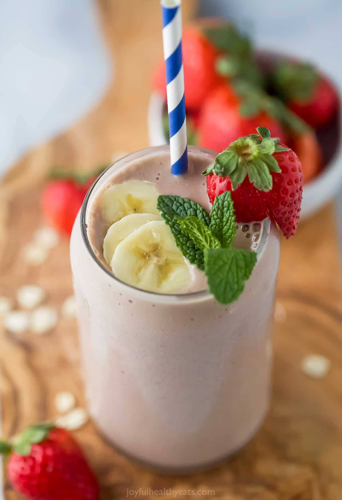 A close-up shot of a strawberry banana smoothie garnished with banana slices, a strawberry and a mint leaf