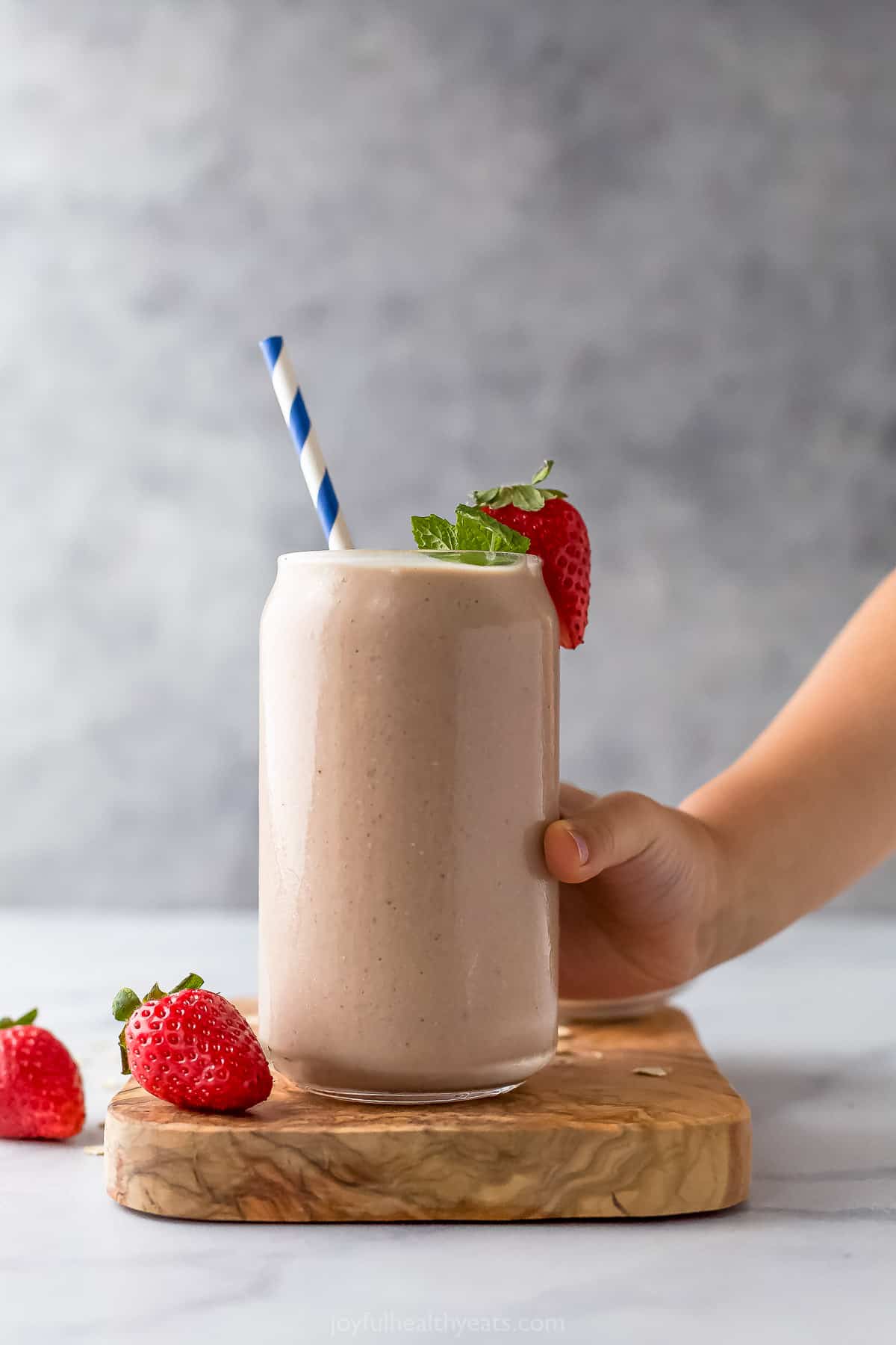 A hand grabbing a strawberry banana smoothie from a wooden cutting board on a countertop