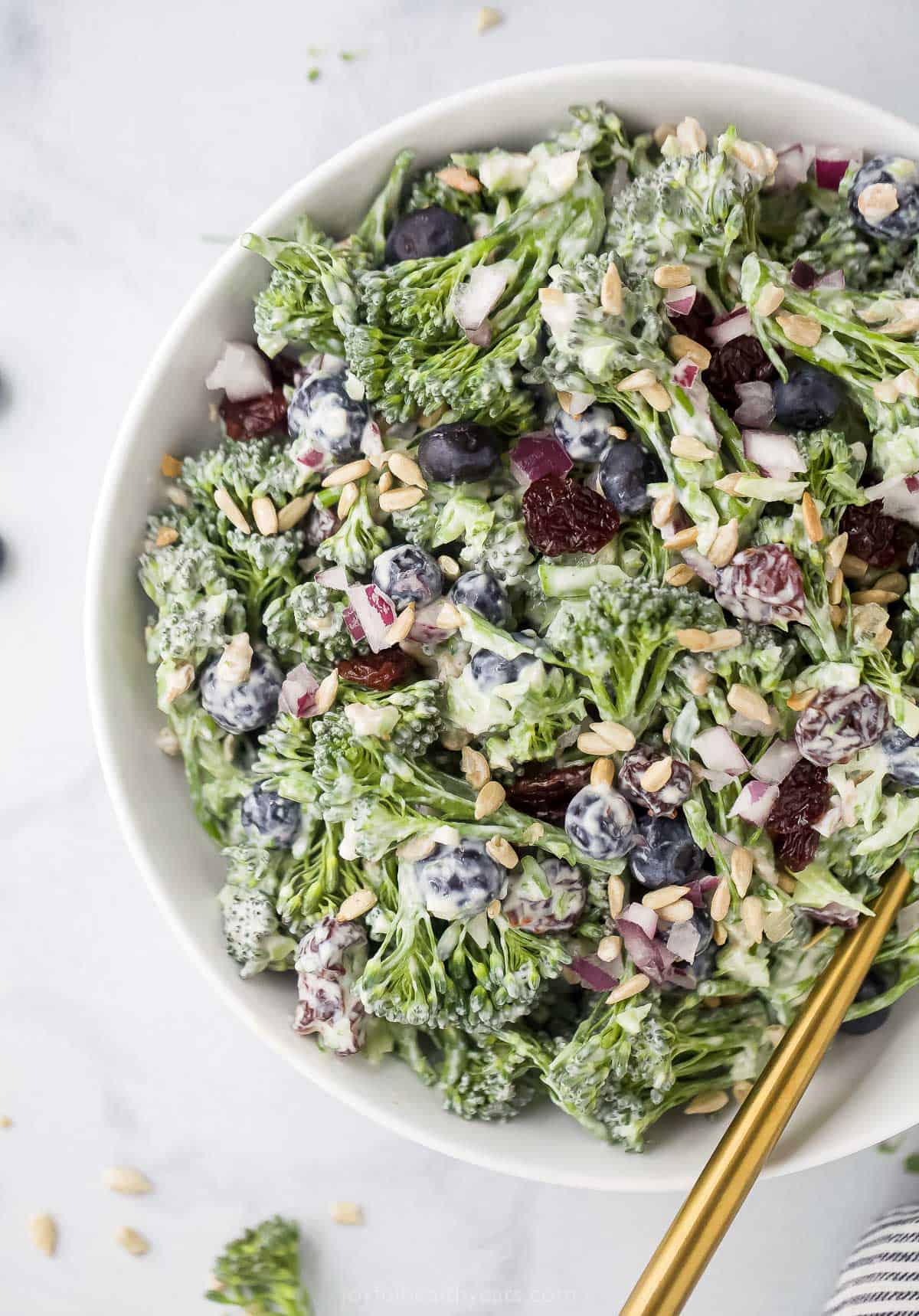 A freshly-tossed broccolini salad inside of a large bowl with a golden serving spoon