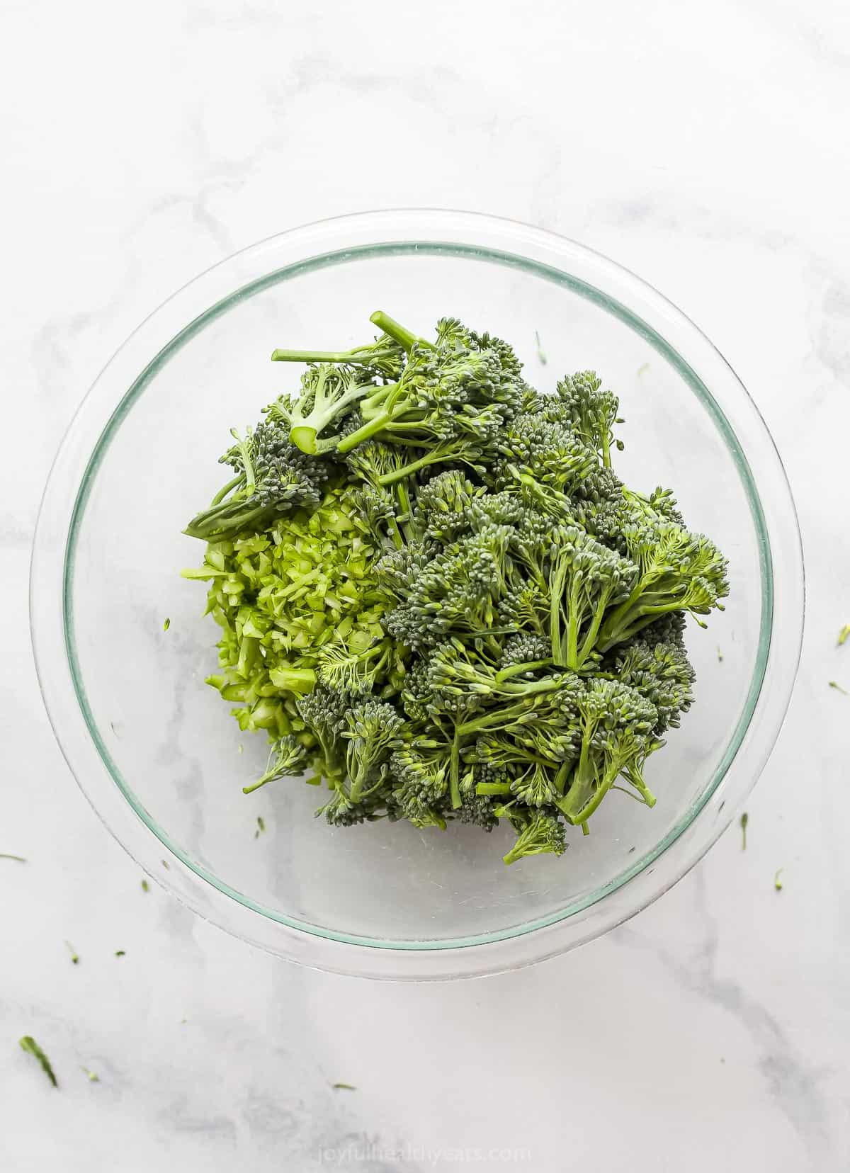 Broccolini florets and chopped up stems inside of a large glass mixing bowl