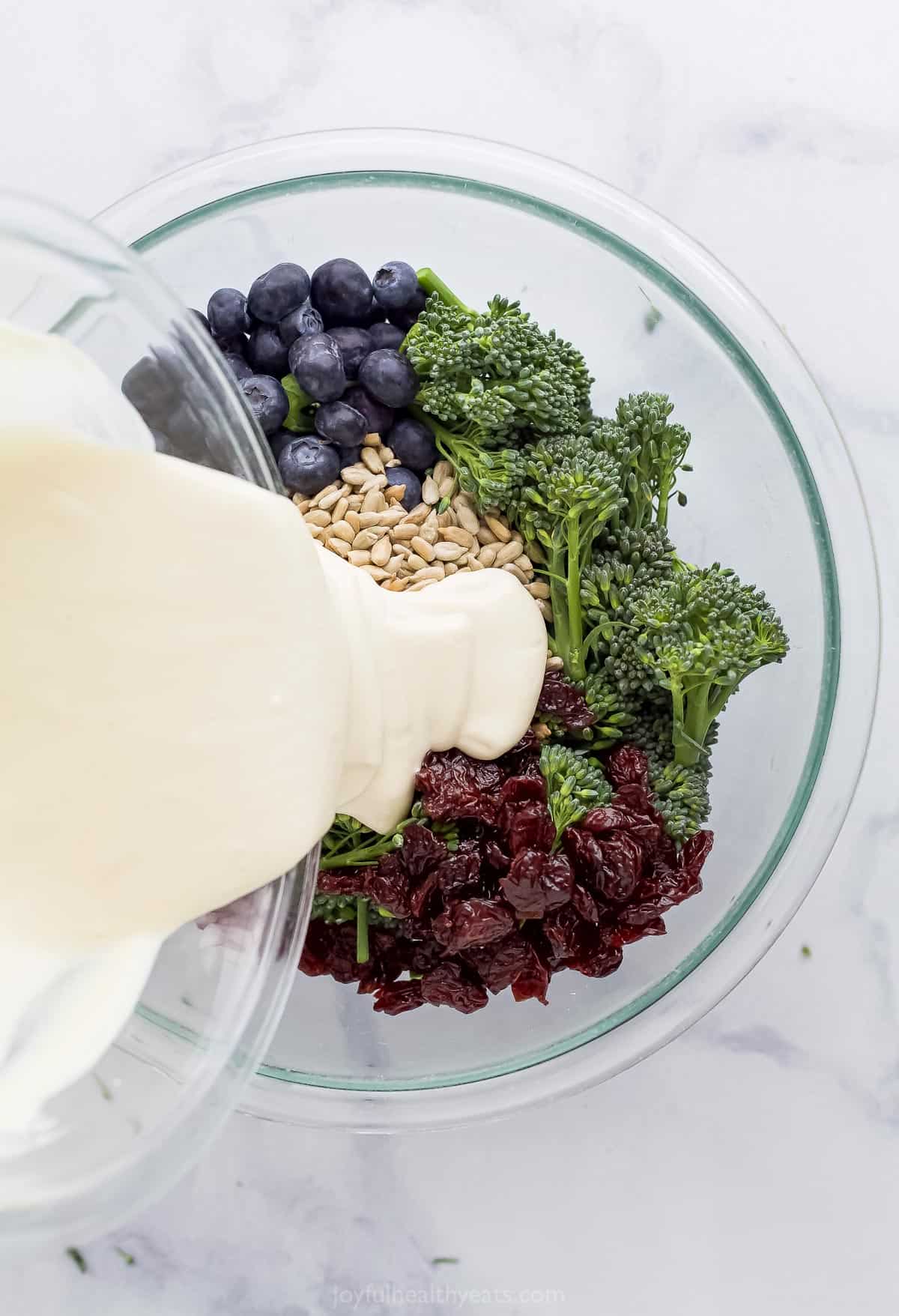 The yogurt dressing being poured over the bowl of broccolini salad ingredients