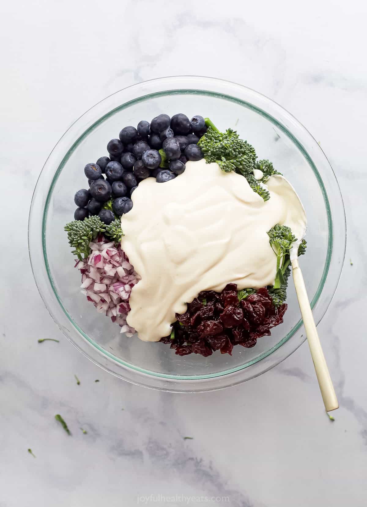 A bowl of broccolini salad with the dressing poured in before the salad has been tossed