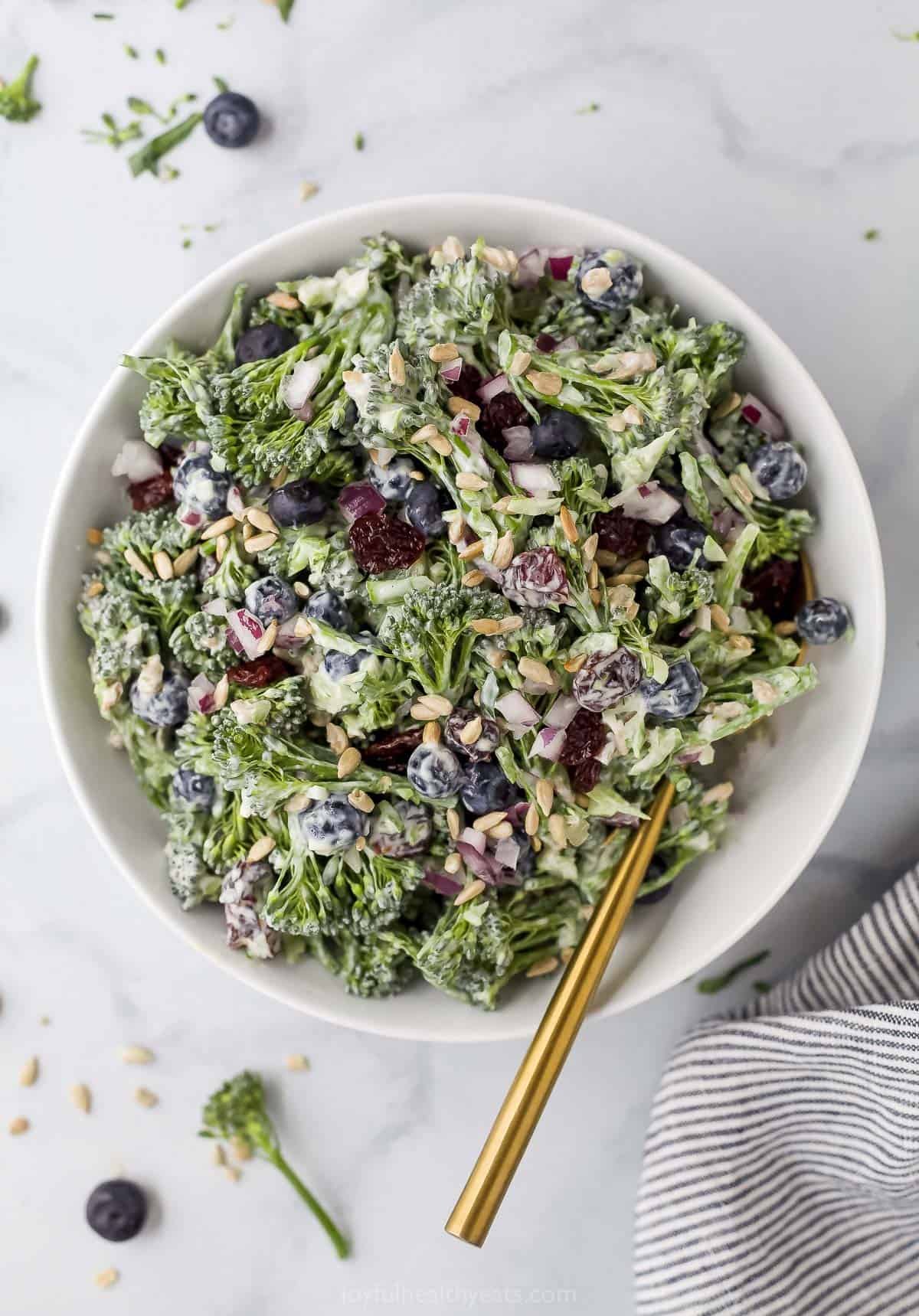 Broccolini salad inside of a large serving bowl beside a striped dishtowel