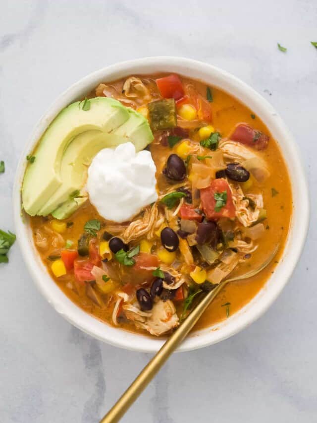 a bowl of chicken enchilada soup with a garnish of sour cream and avocado slices