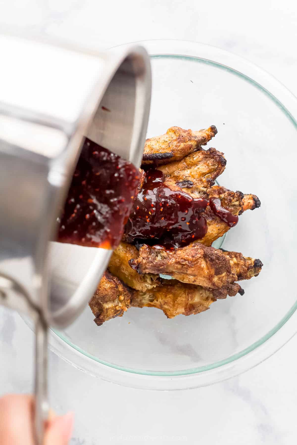 raspberry hoisin glaze being poured over baked chicken wings