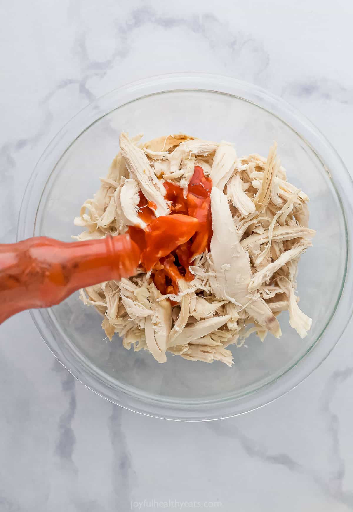 hot sauce being poured on shredded chicken