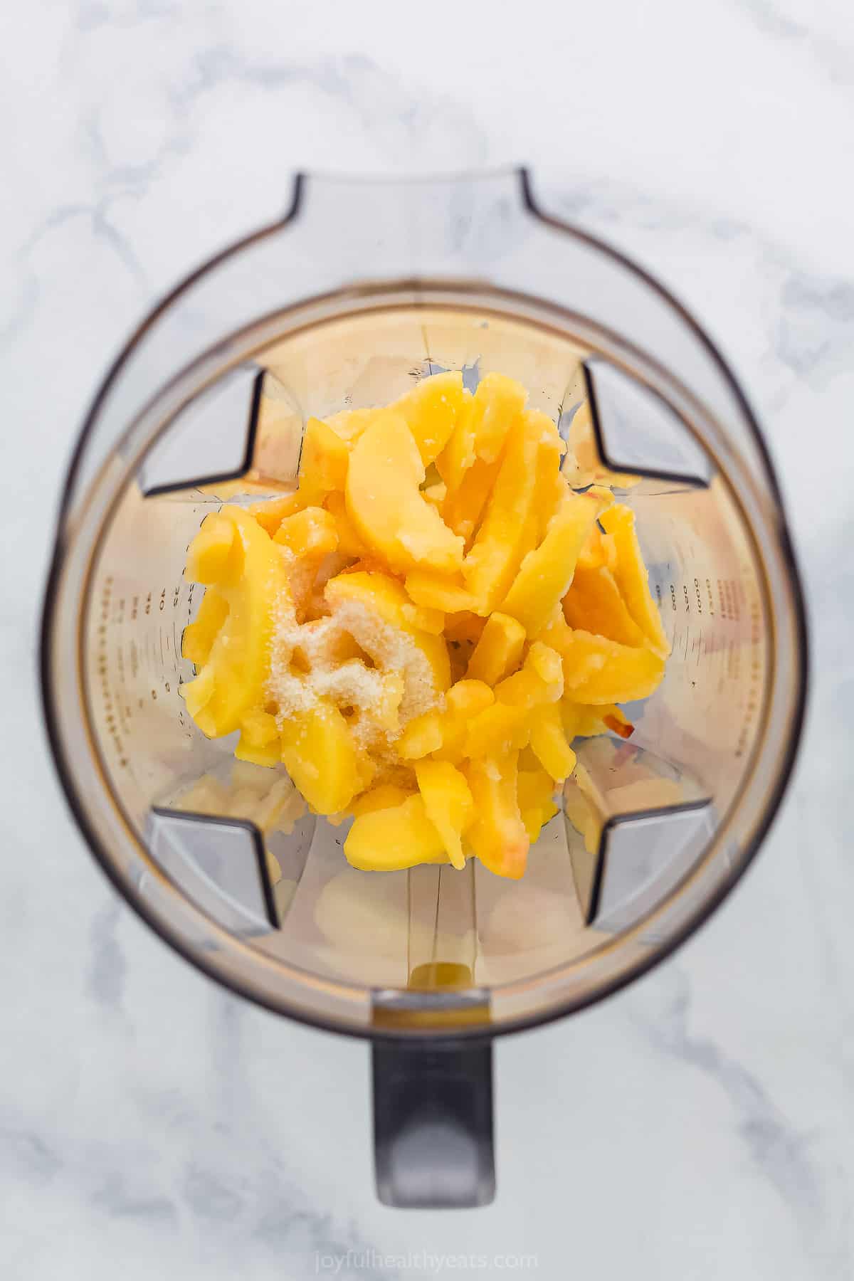 Peaches and table sugar inside of a blender on a kitchen countertop