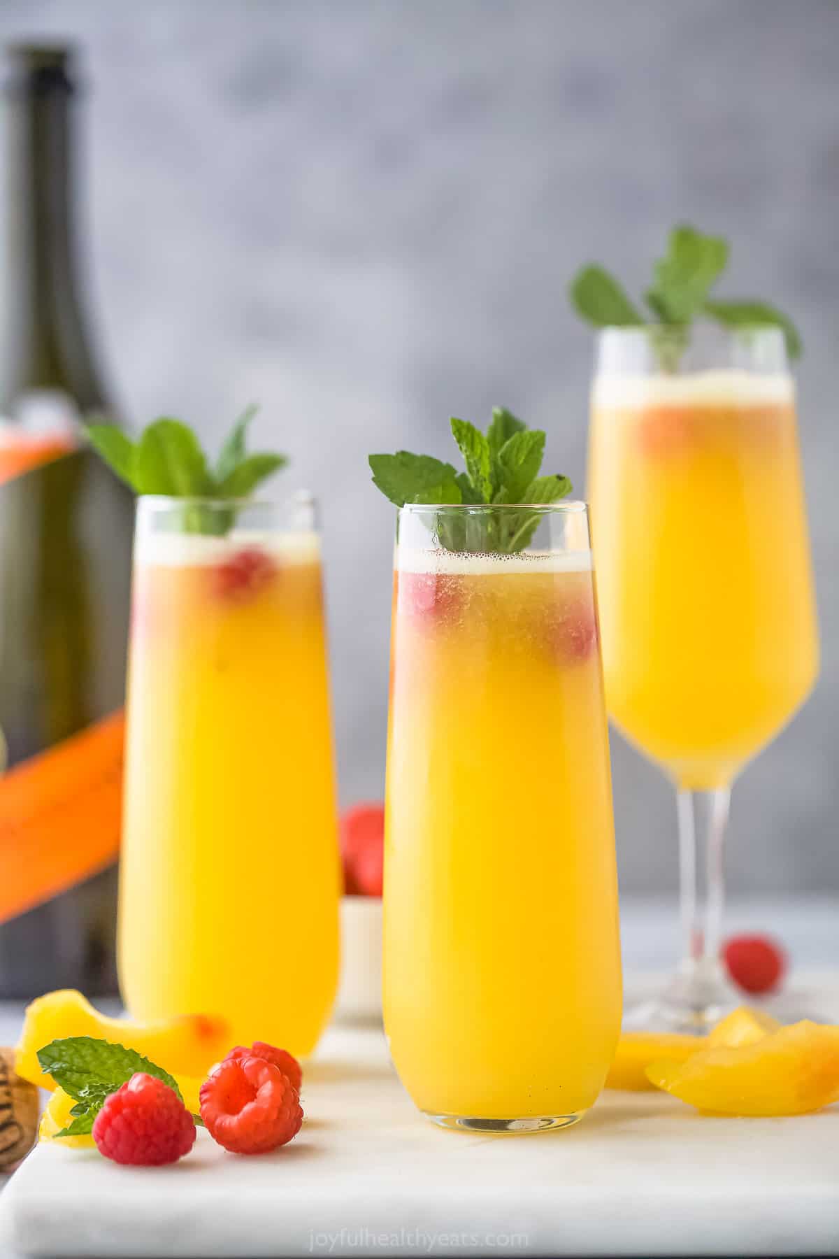 Three peach bellinis on a cutting board with a bottle of prosecco in the background