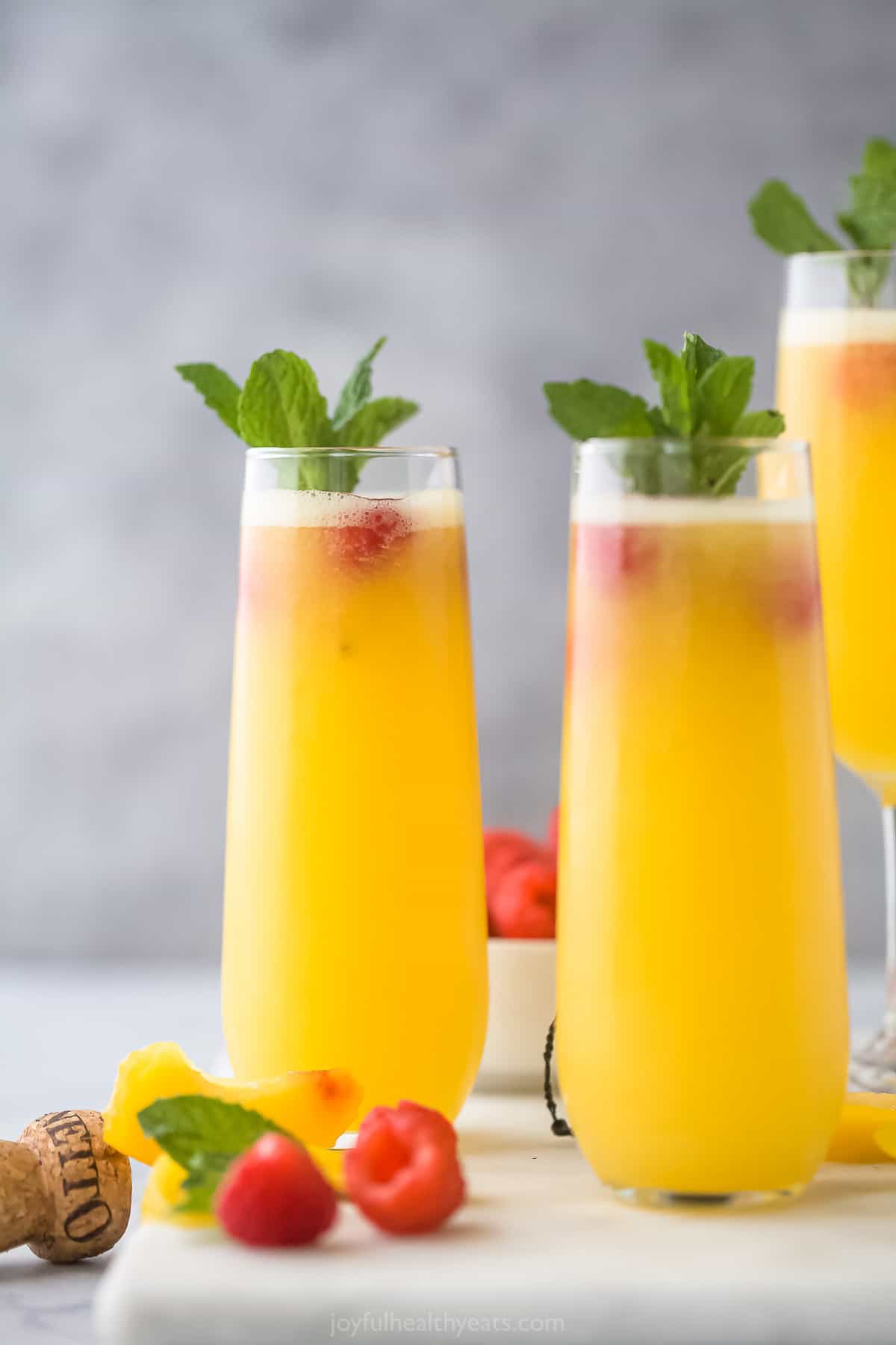 Two peach bellinis garnished with fresh raspberries and mint sprigs
