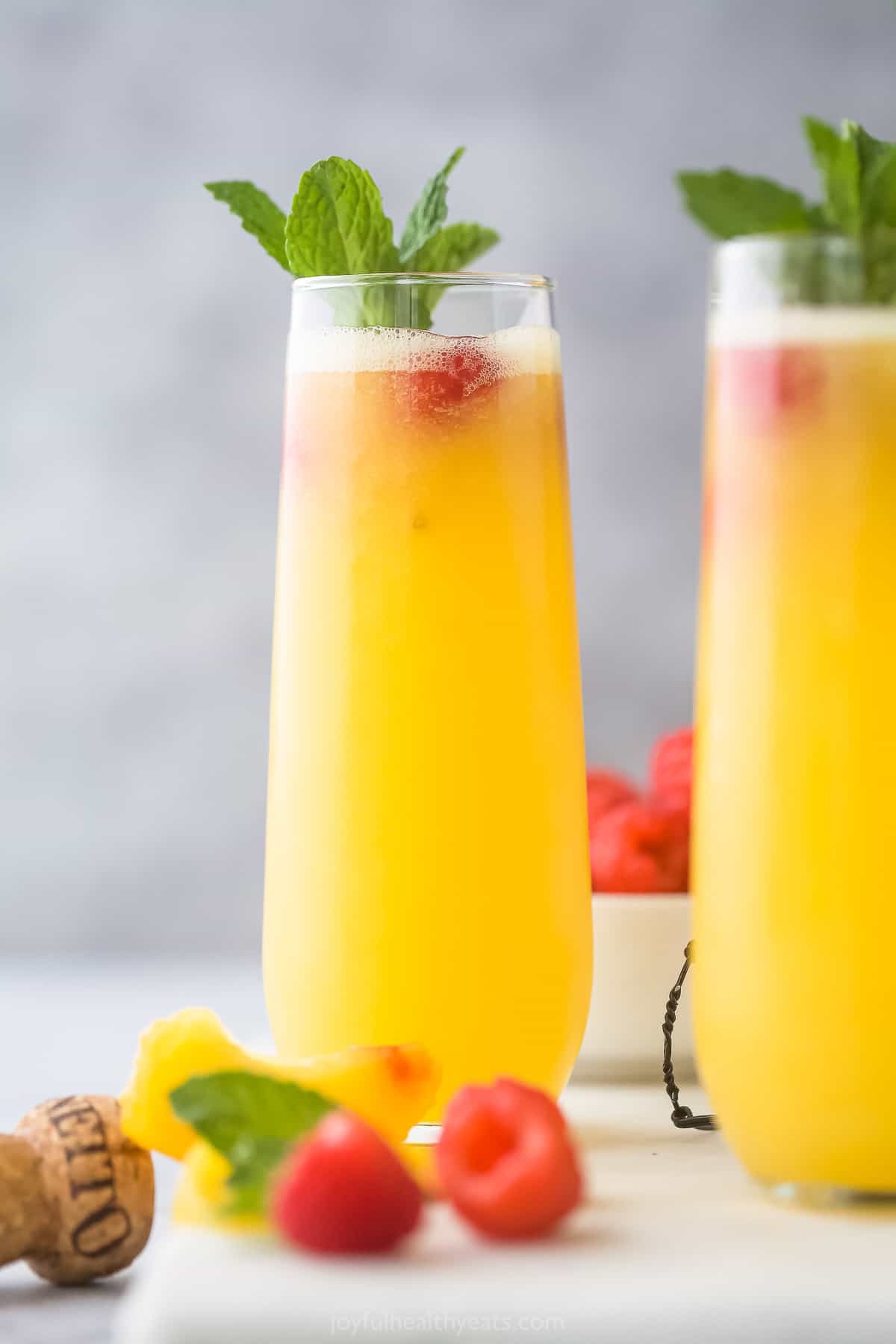 Two homemade bellinis with a cork and fresh fruit in the foreground