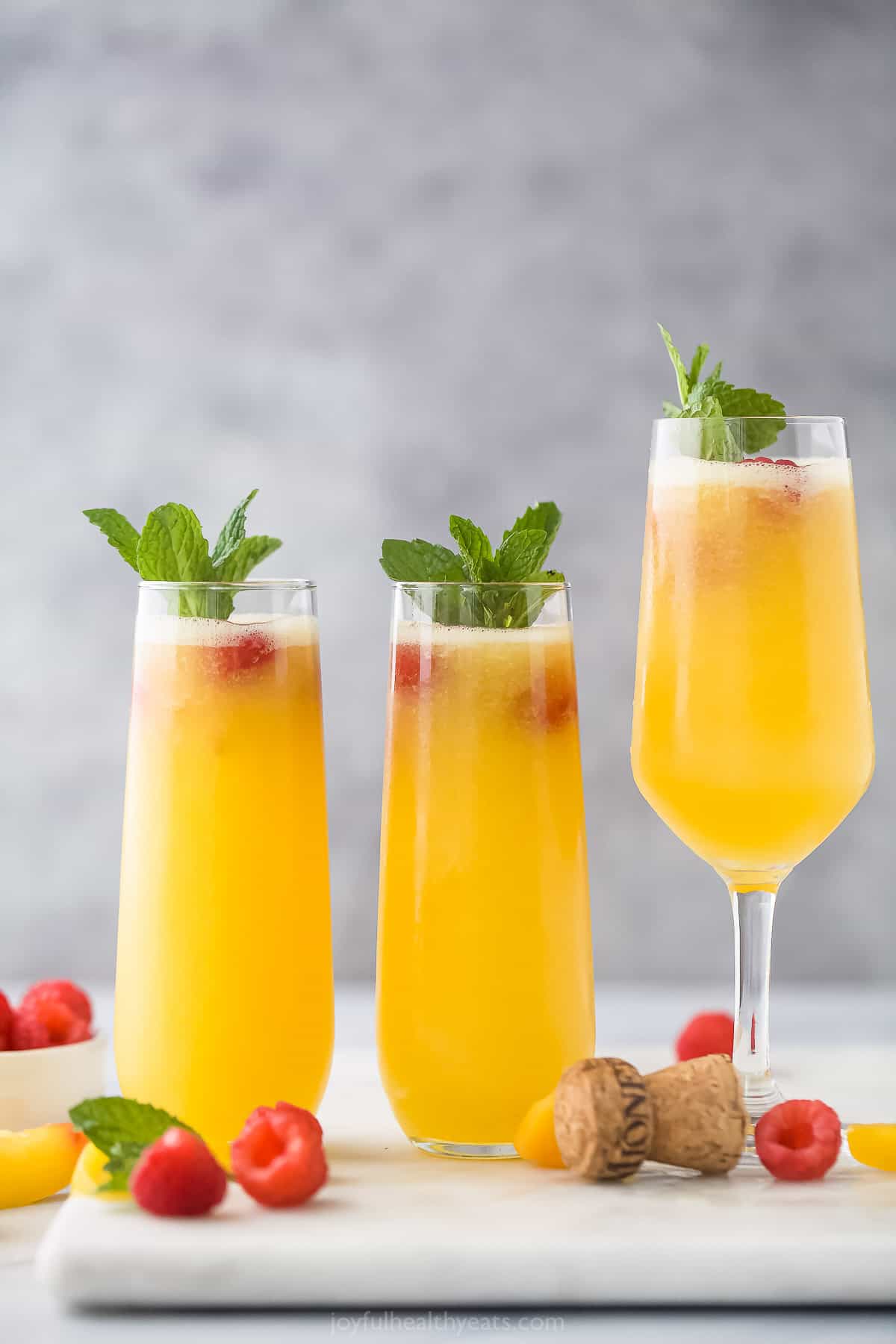 Three peach bellinis in different cocktail glasses on a marble kitchen countertop