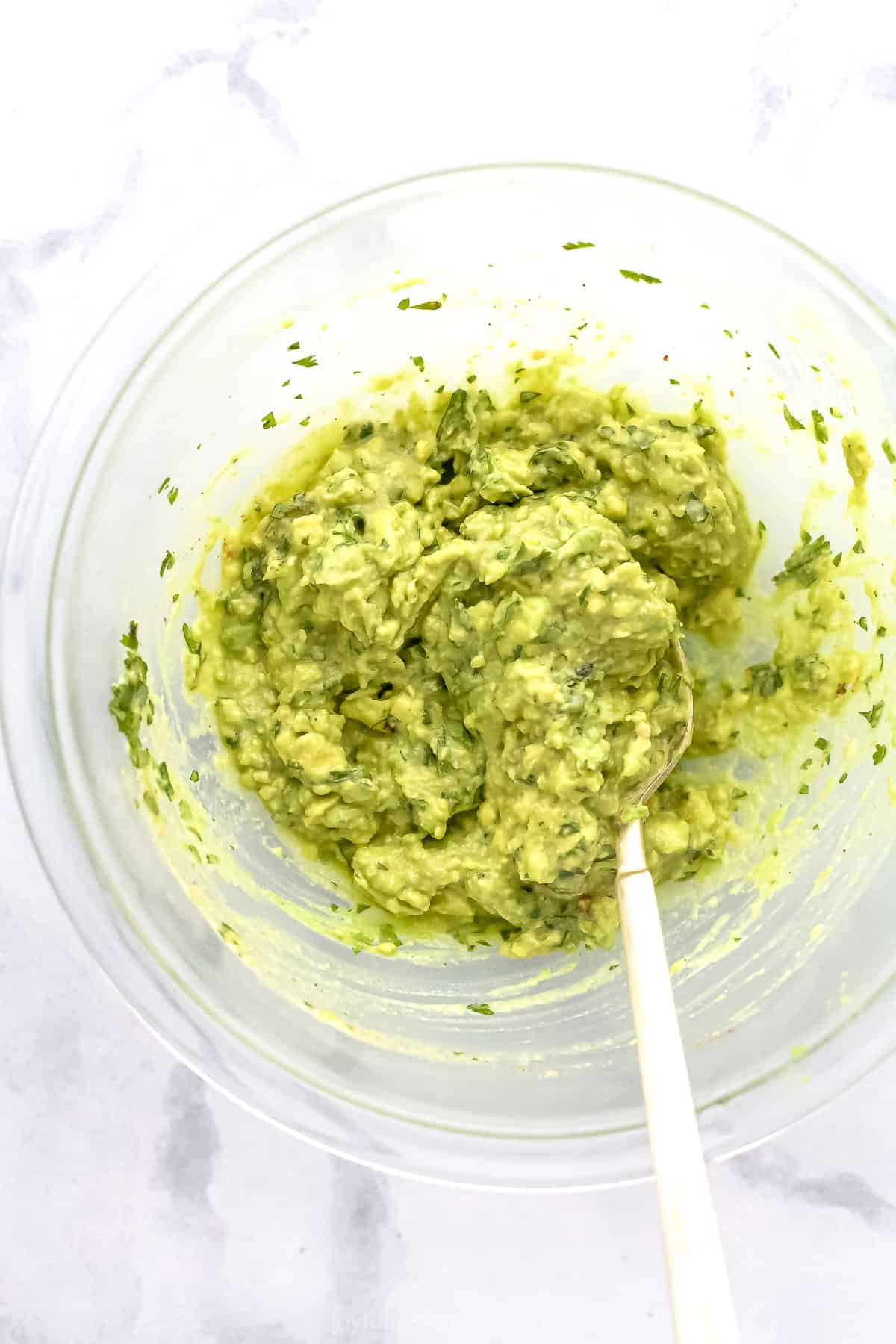 Guacamole being mixed with a spoon in a glass mixing bowl