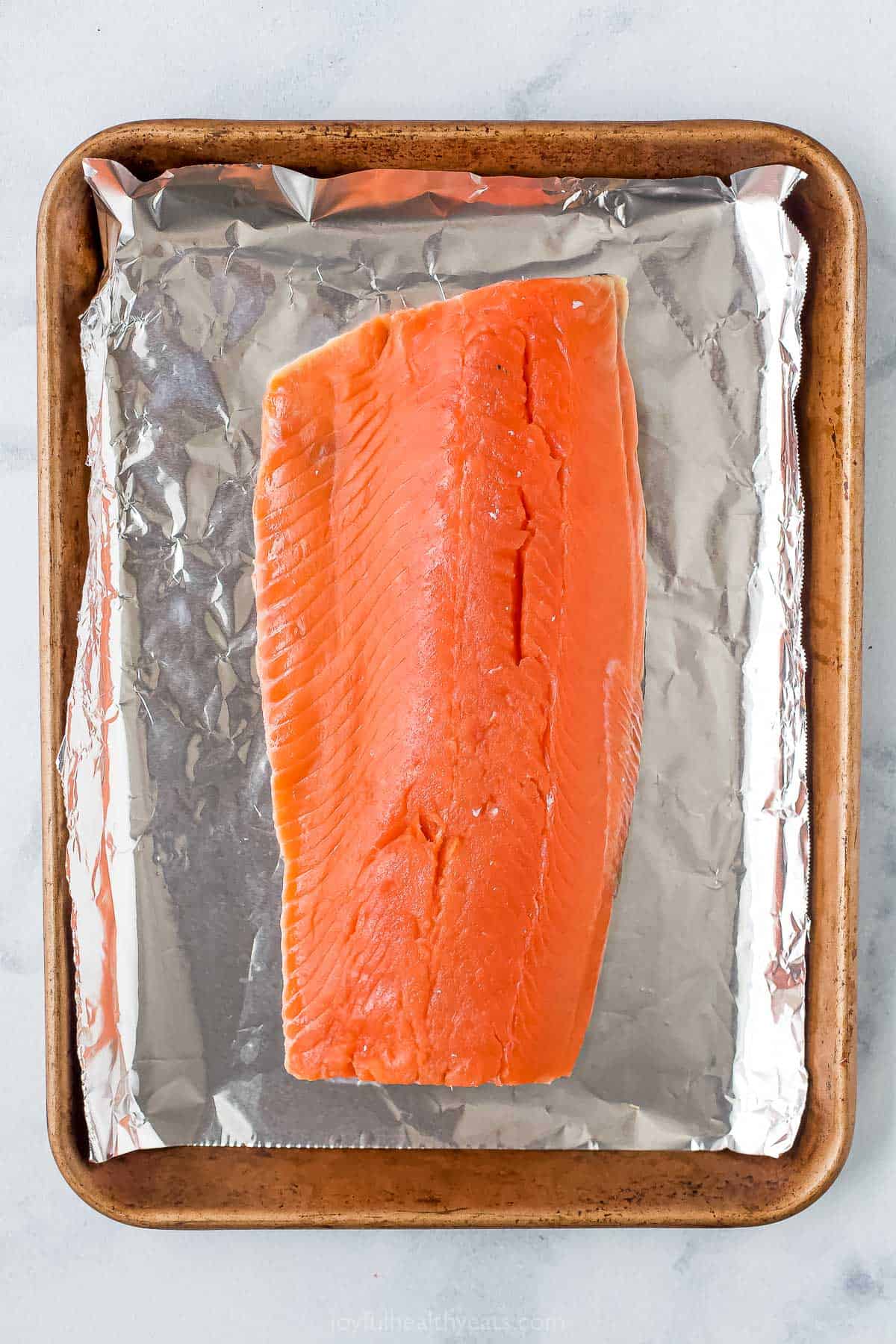 A raw salmon fillet on a baking tray lined with a sheet of aluminum foil.