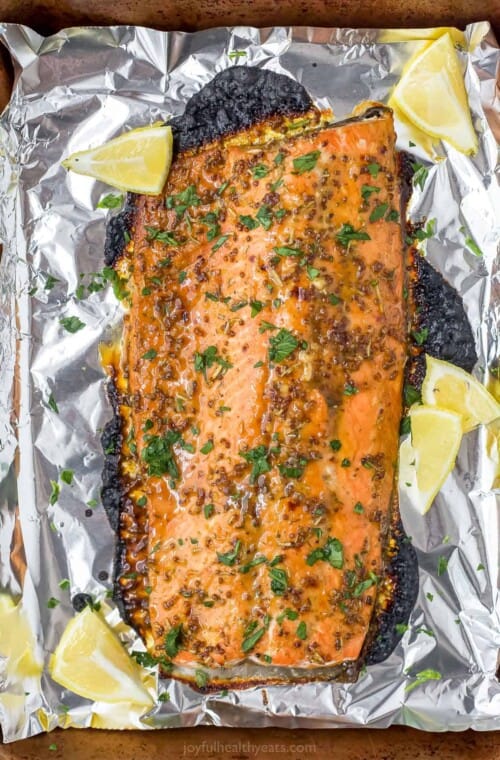 A foil-lined baking sheet with a baked Dijon maple glazed salmon fillet on top of it