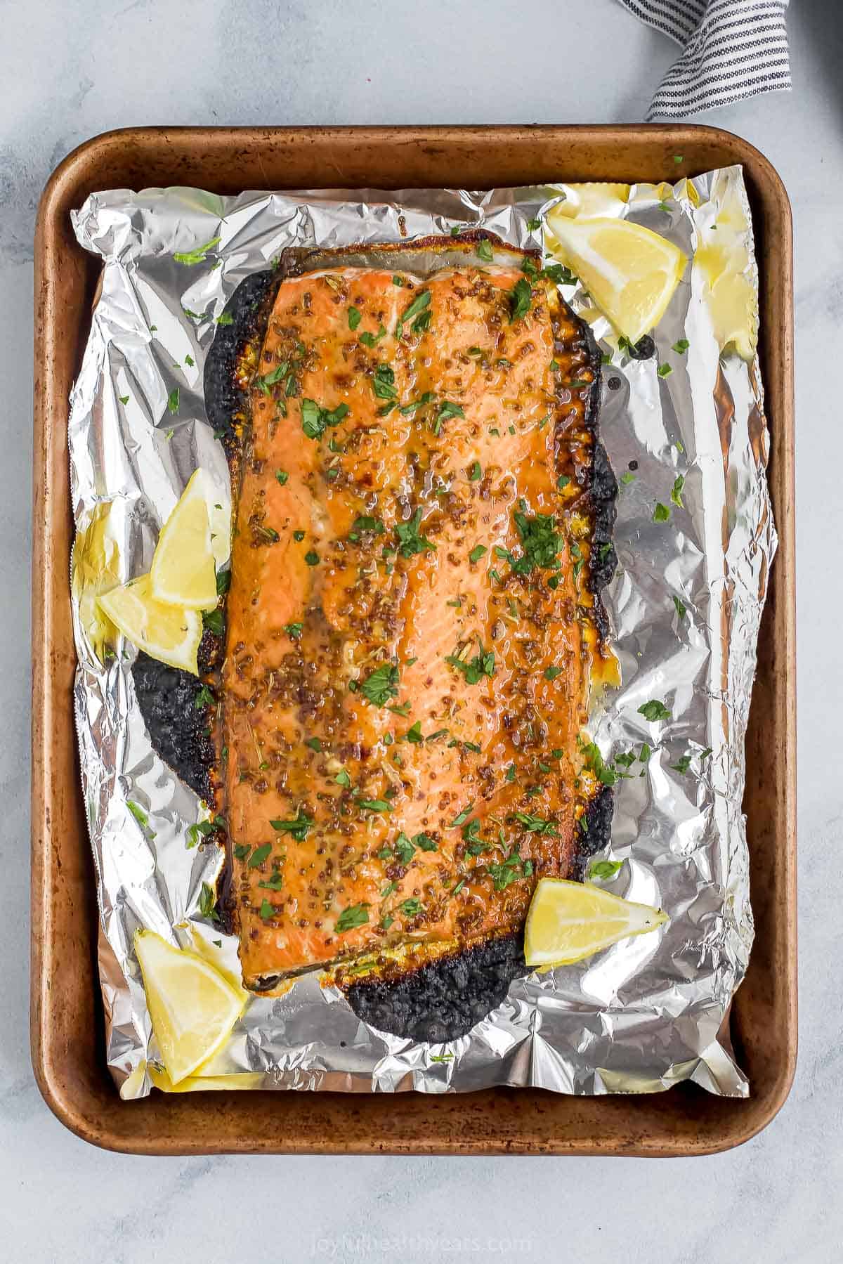 A baked salmon fillet on a cookie sheet lined with foil on top of a marble surface