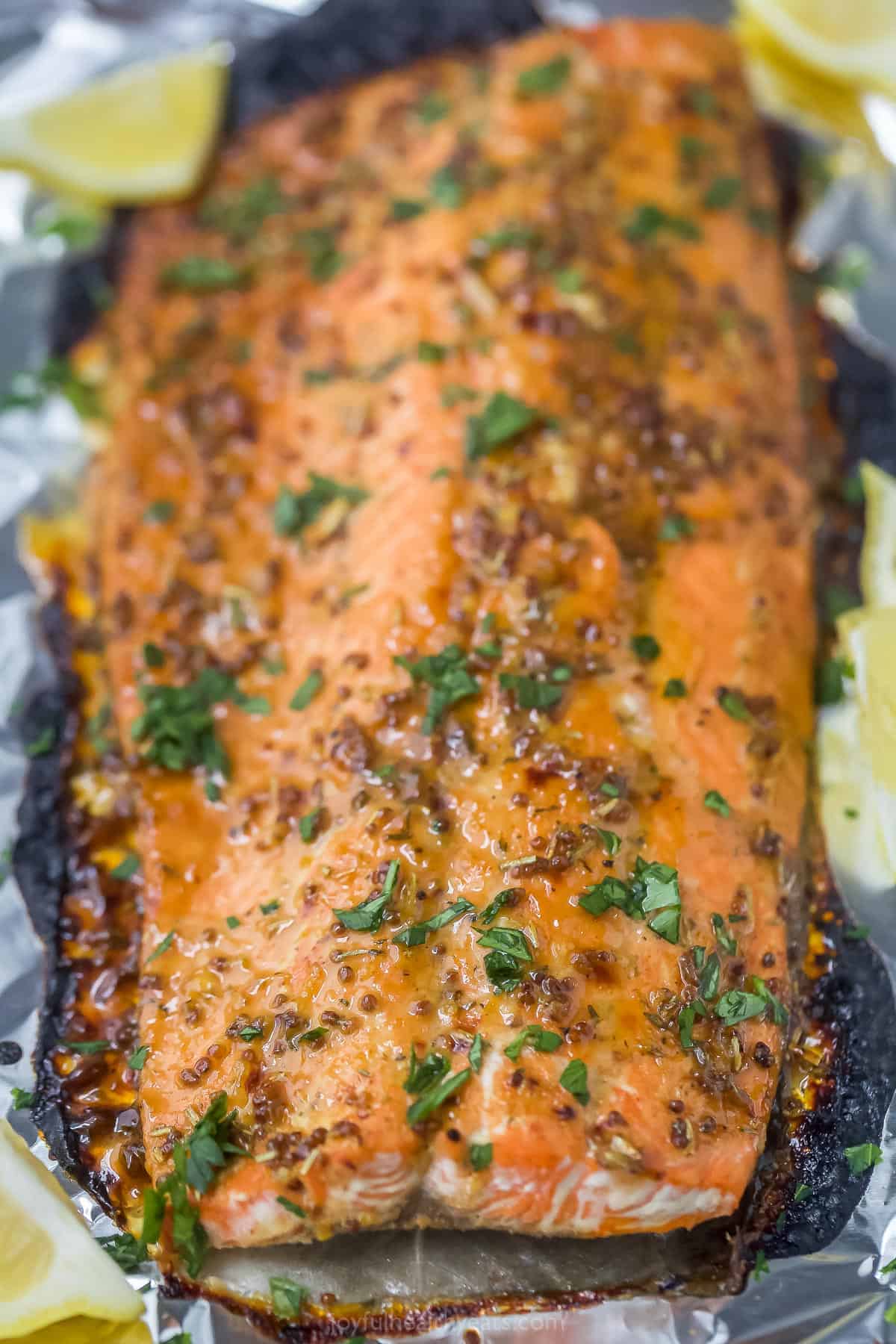 Dijon maple glazed salmon is a low-calorie, high-protein dinner that's done in just 15 minutes! The tangy-sweet glaze caramelizes the skin while the inside bakes to tender, flaky perfection. A close-up shot of a baked salmon fillet topped with fresh chopped parsley.