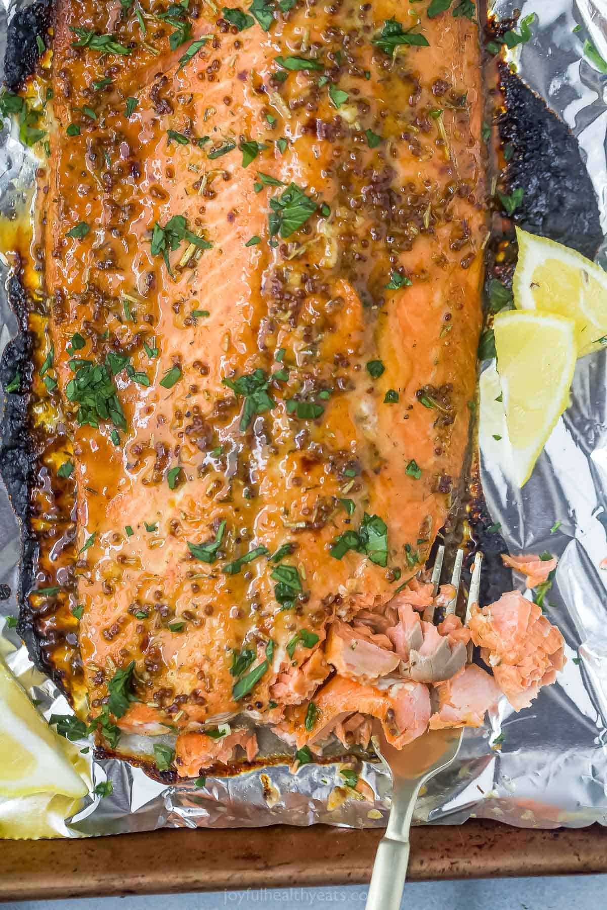 A roasted salmon fillet on top of a sheet of aluminum foil with one bite on a metal fork.