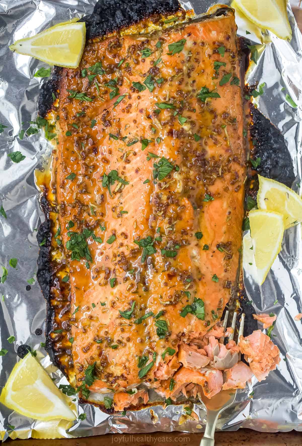 Dijon maple glazed salmon is a low-calorie, high-protein dinner that's done in just 15 minutes! The tangy-sweet glaze caramelizes the skin while the inside bakes to tender, flaky perfection. A Dijon maple glazed salmon fillet on a baking sheet with five lemon wedges beside it.