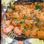 A baked salmon fillet on top of a foil-lined baking sheet with a fork flaking some meat off of the fillet