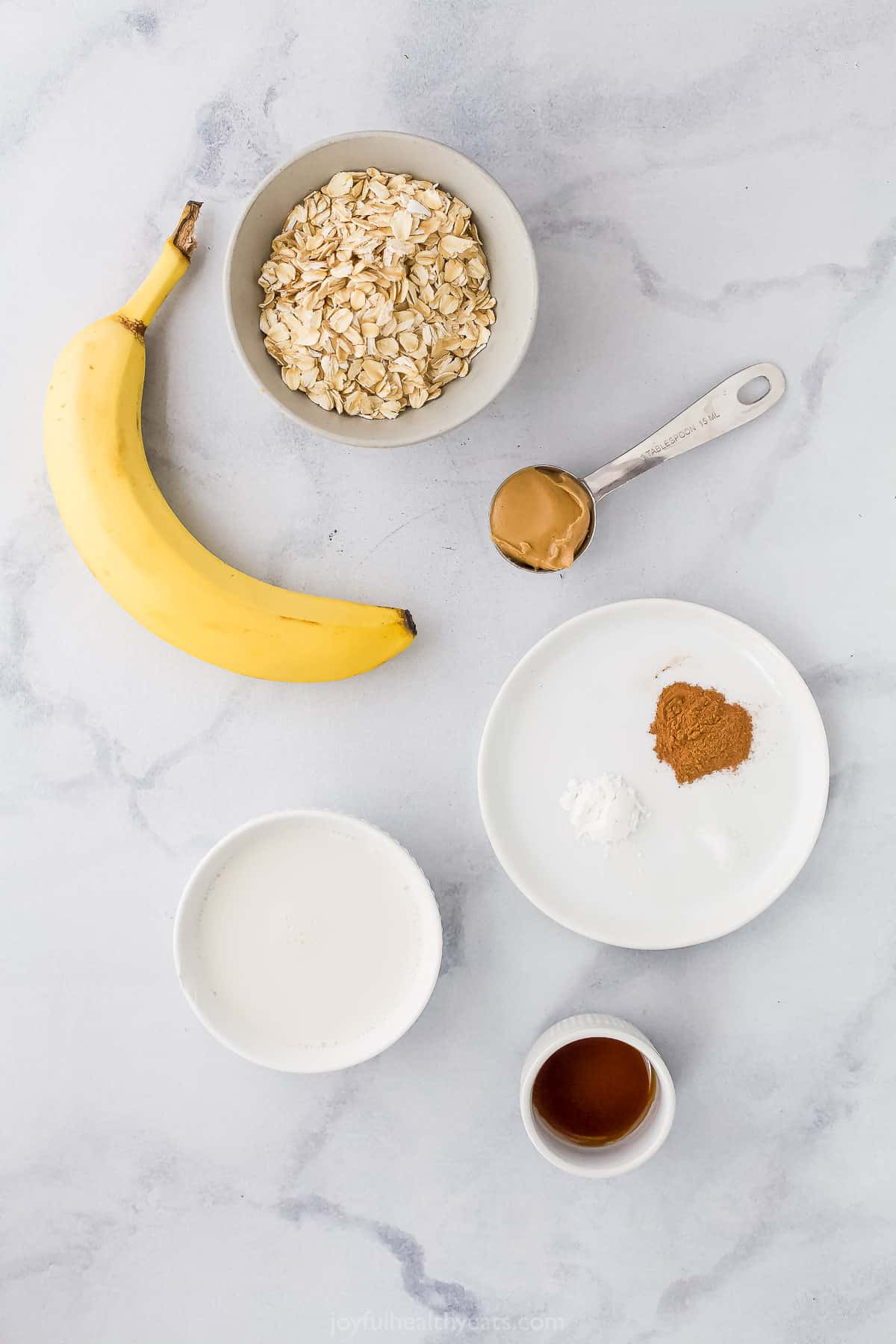 A fresh banana, a bowl of oats, cinnamon and the rest of the chocolate peanut butter baked oatmeal ingredients on a countertop