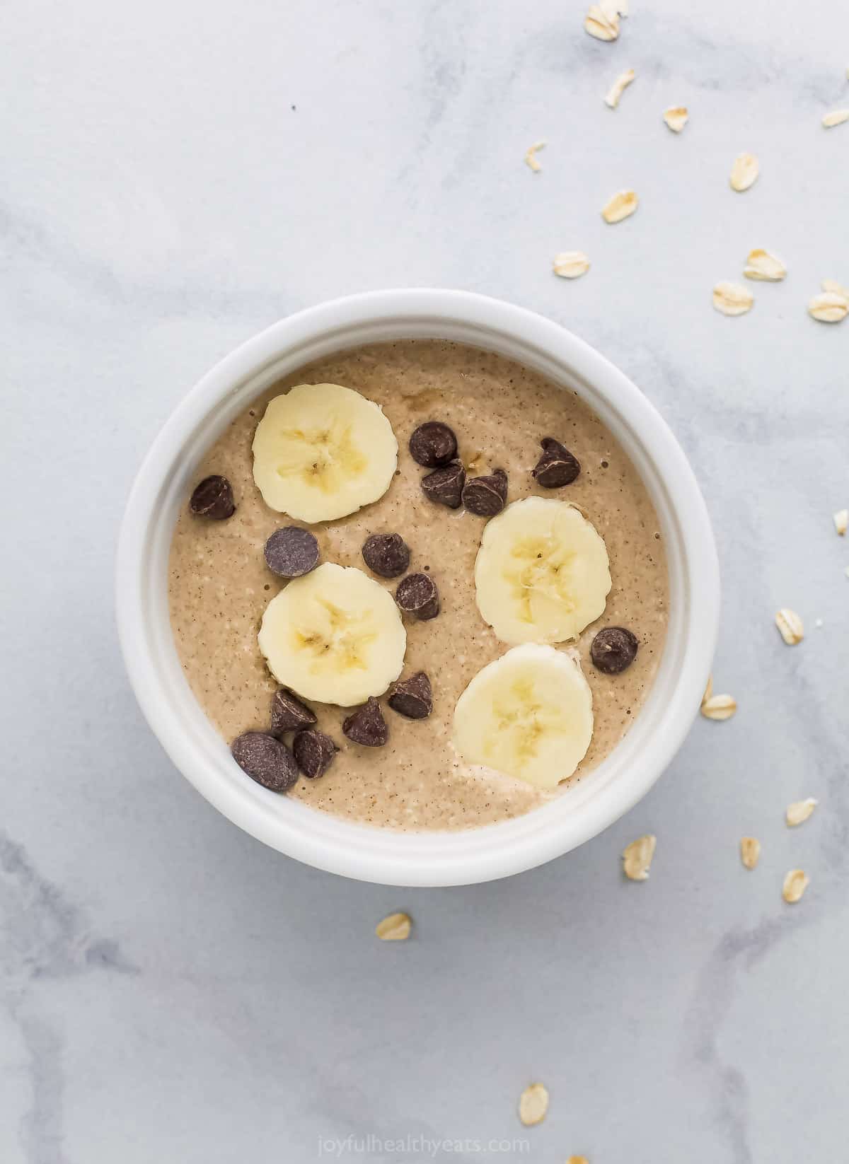 The oat mixture inside of a ramekin with chocolate chips and fresh banana slices on the surface