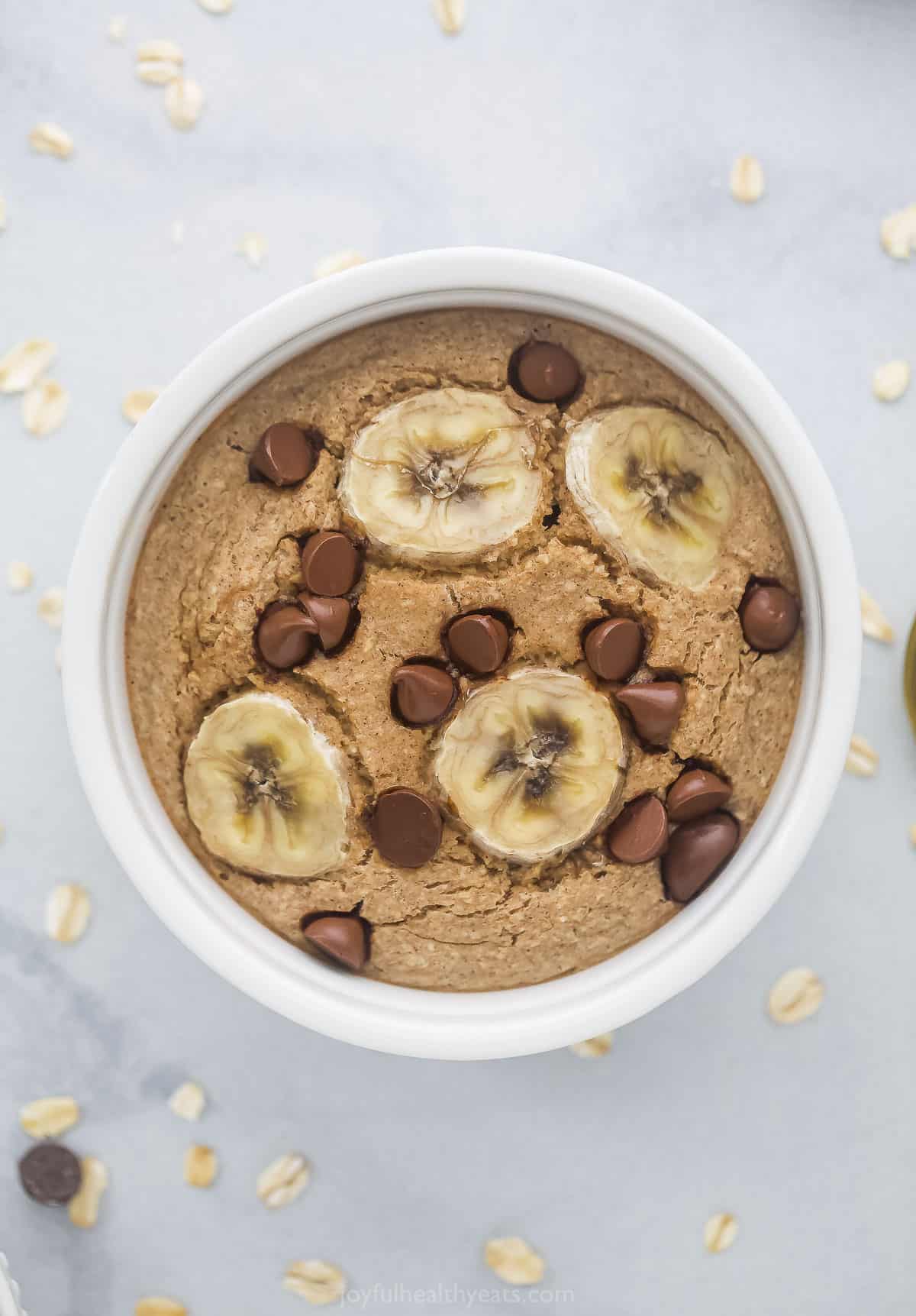 A ramekin full of baked oatmeal with chocolate chips and banana slices on top
