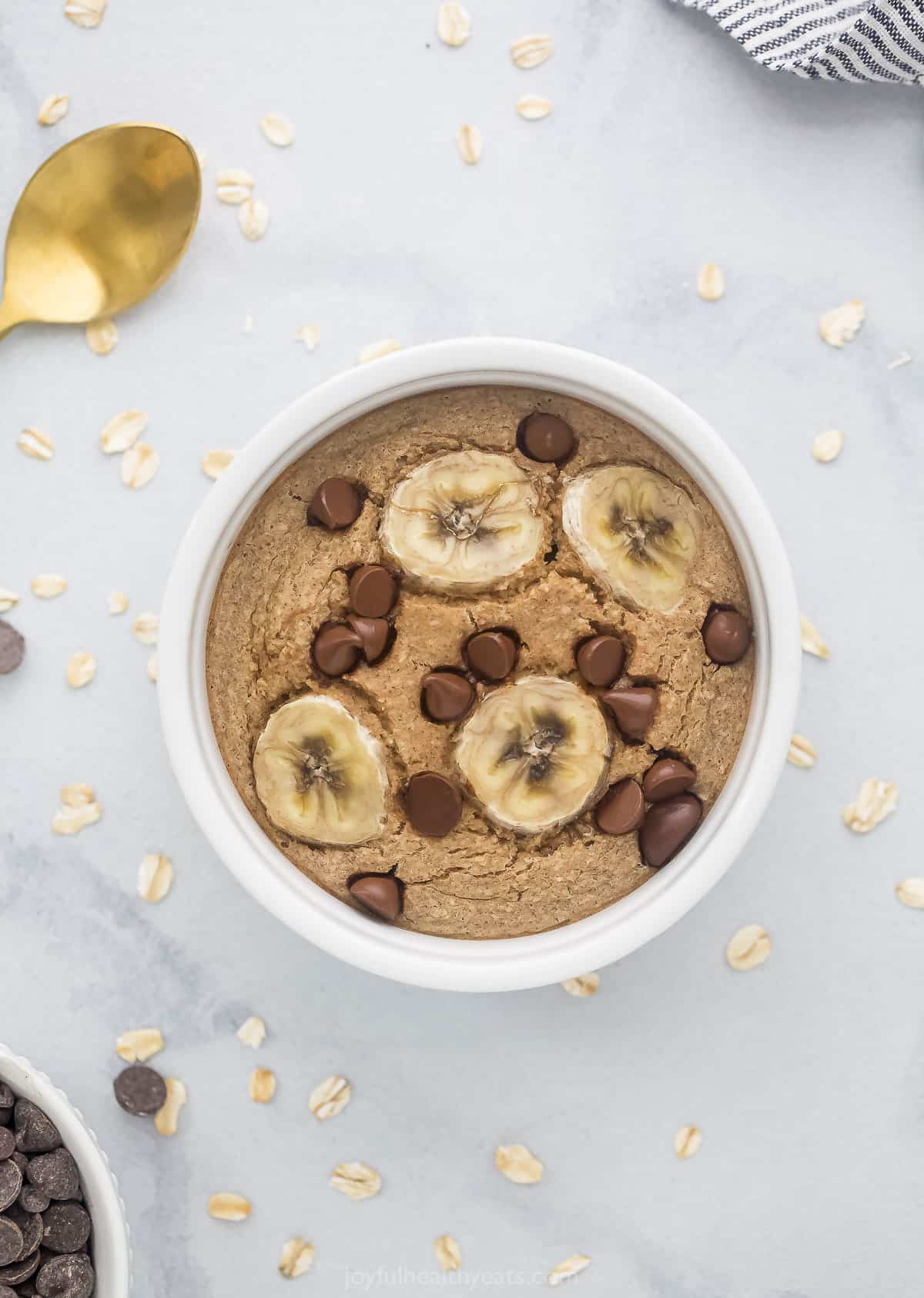 A ramekin full of baked oats on a marble countertop with a bowl of chocolate chips beside it