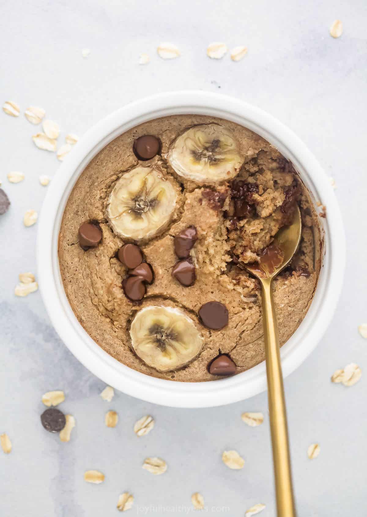 A serving of baked oats in a ramekin on a countertop with a golden spoon digging into the oatmeal