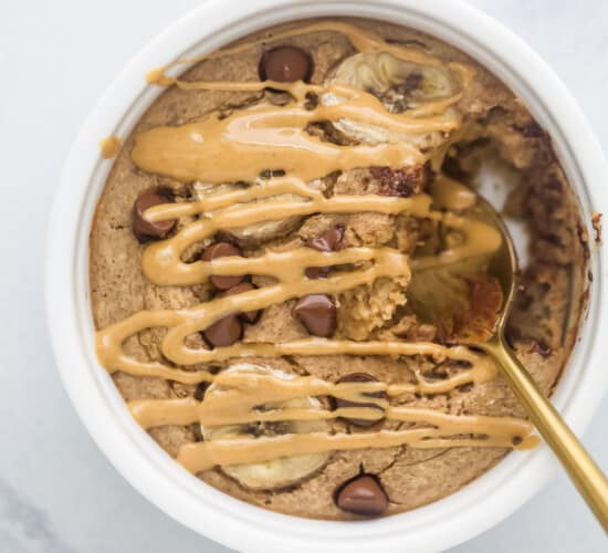 Warm baked oatmeal inside of a ramekin with a drizzle of melty peanut butter on top