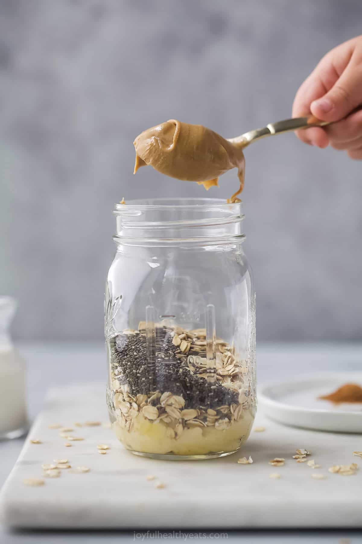 A spoon of peanut butter over a mason jar of oats