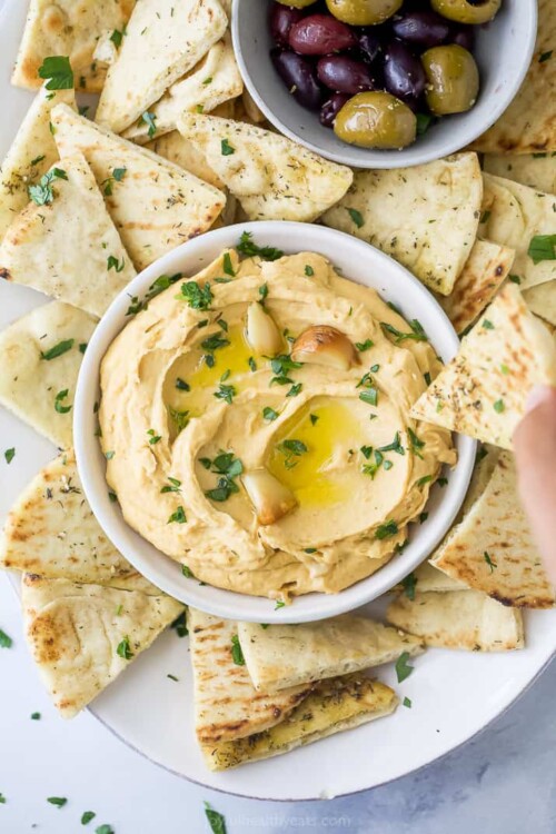 roasted garlic hummus in a bowl with pita chips around it