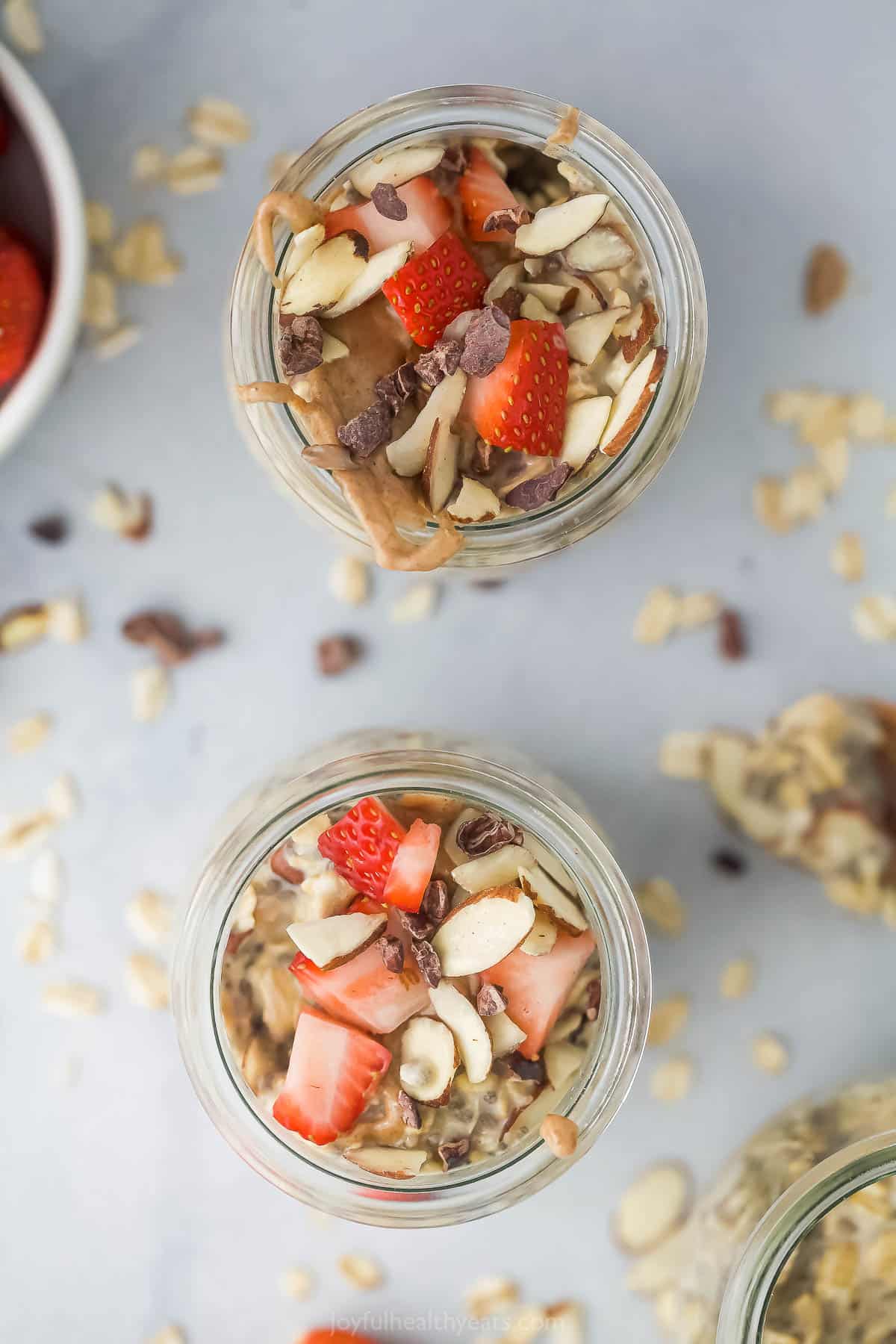 Two jars of vanilla almond oatmeal topped with strawberry slices, almond butter and cacao nibs