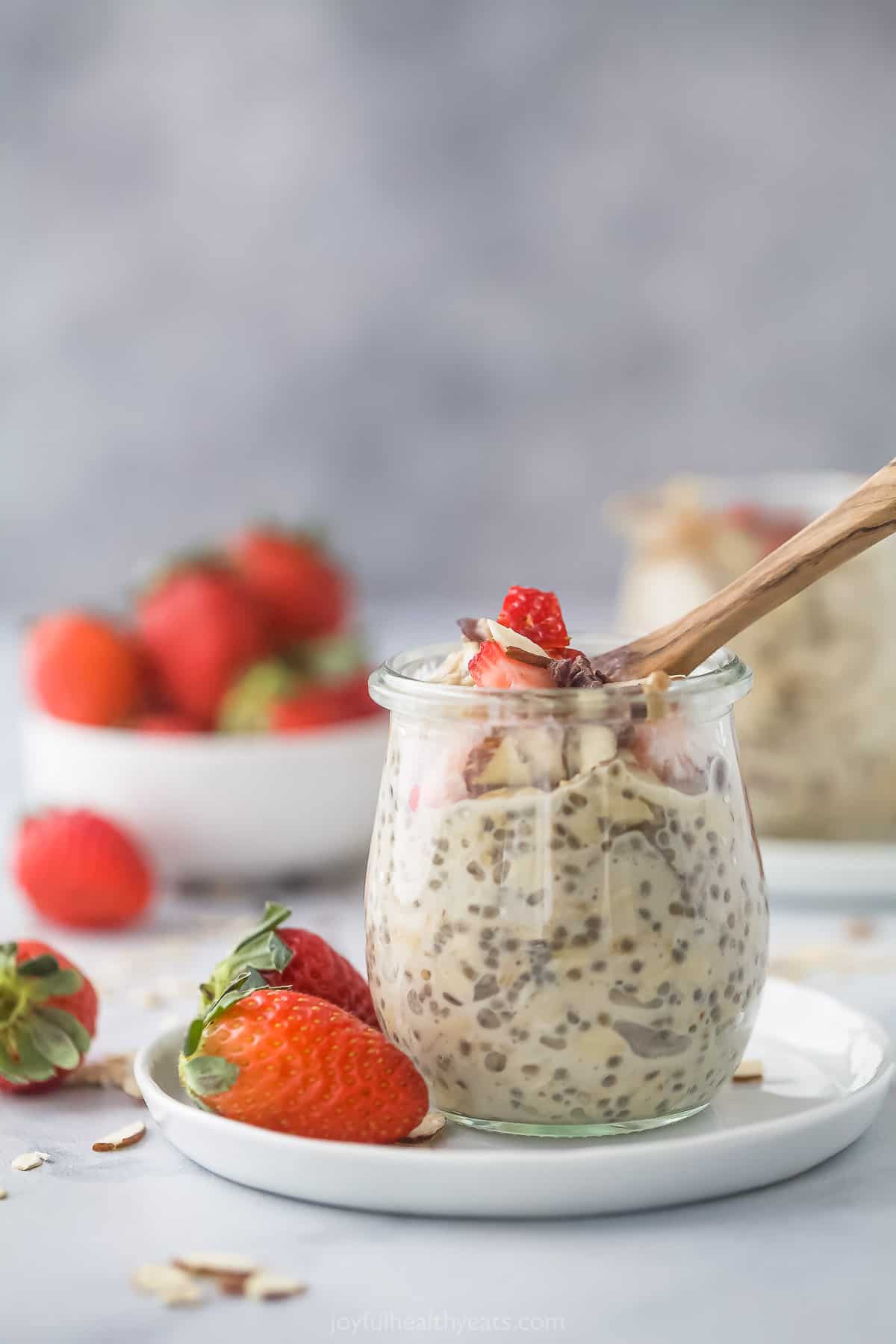 A jar of vanilla almond oatmeal on a plate with two fresh strawberries