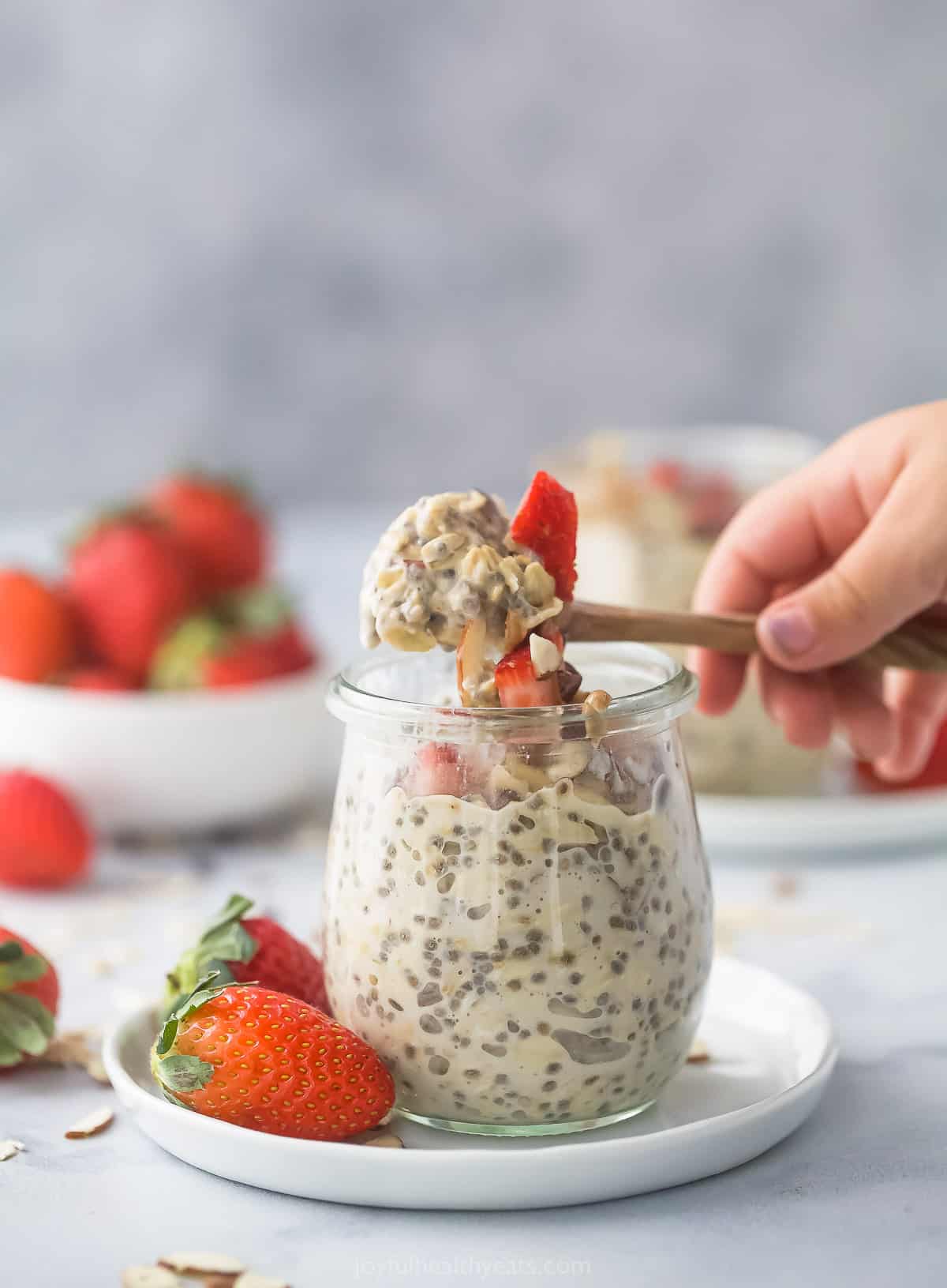 A wooden spoon holding a bite of overnight oatmeal over a glass jar on a plate