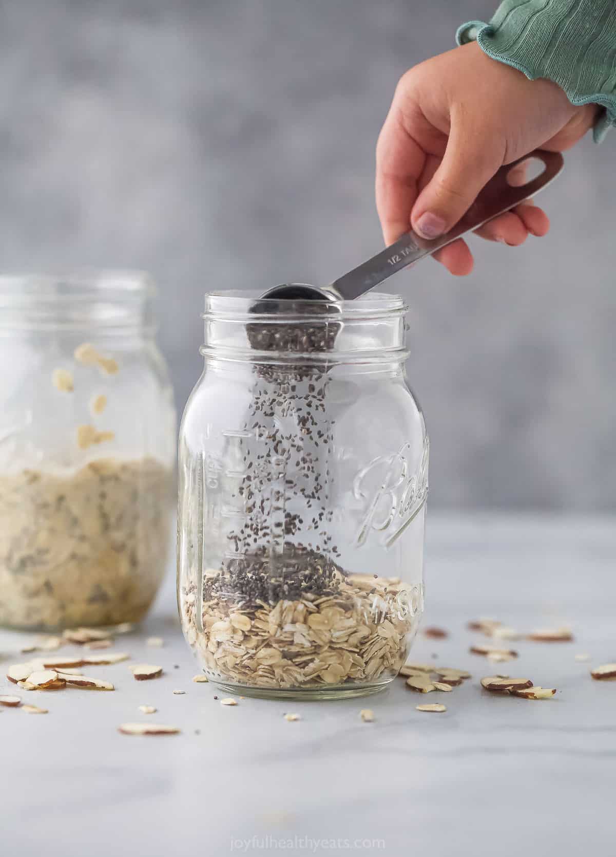 Chia seeds being poured into a glass jar containing rolled oats