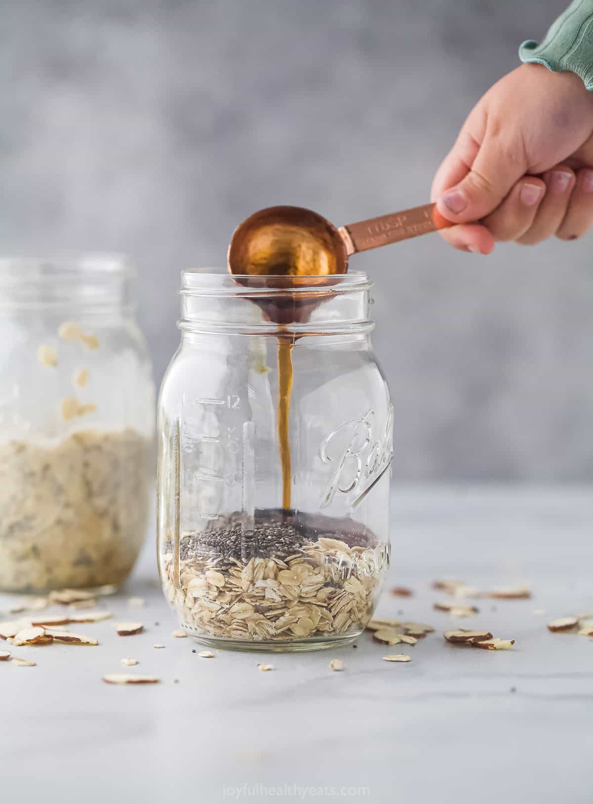 A tablespoon of pure maple syrup being poured into a jar full of chia seeds and old-fashioned oats