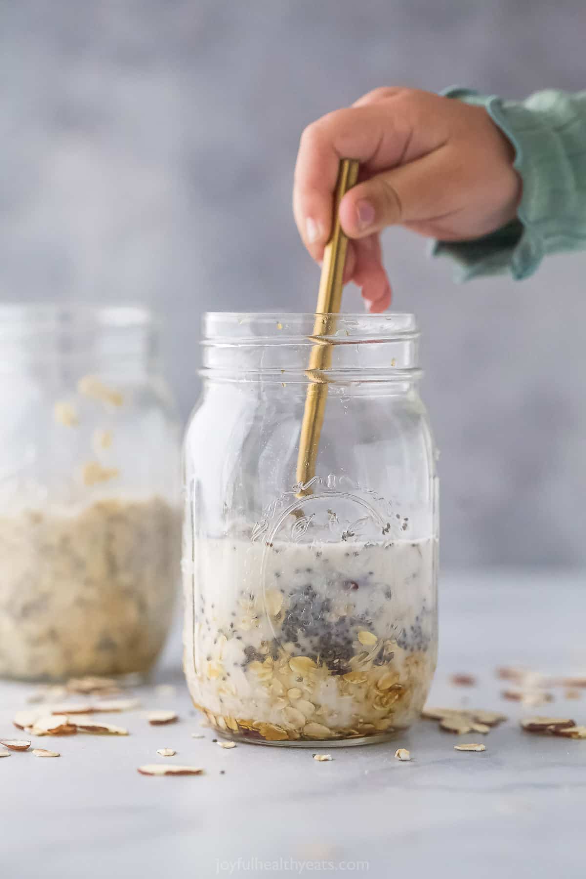 A jar full of almond milk, chia seeds, rolled oats and the rest of the ingredients being stirred with a long spoon