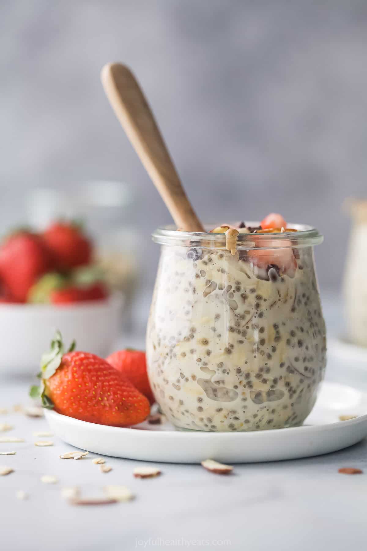 Vanilla almond overnight oats in a jar on a plate with a bunch of fresh berries in the background