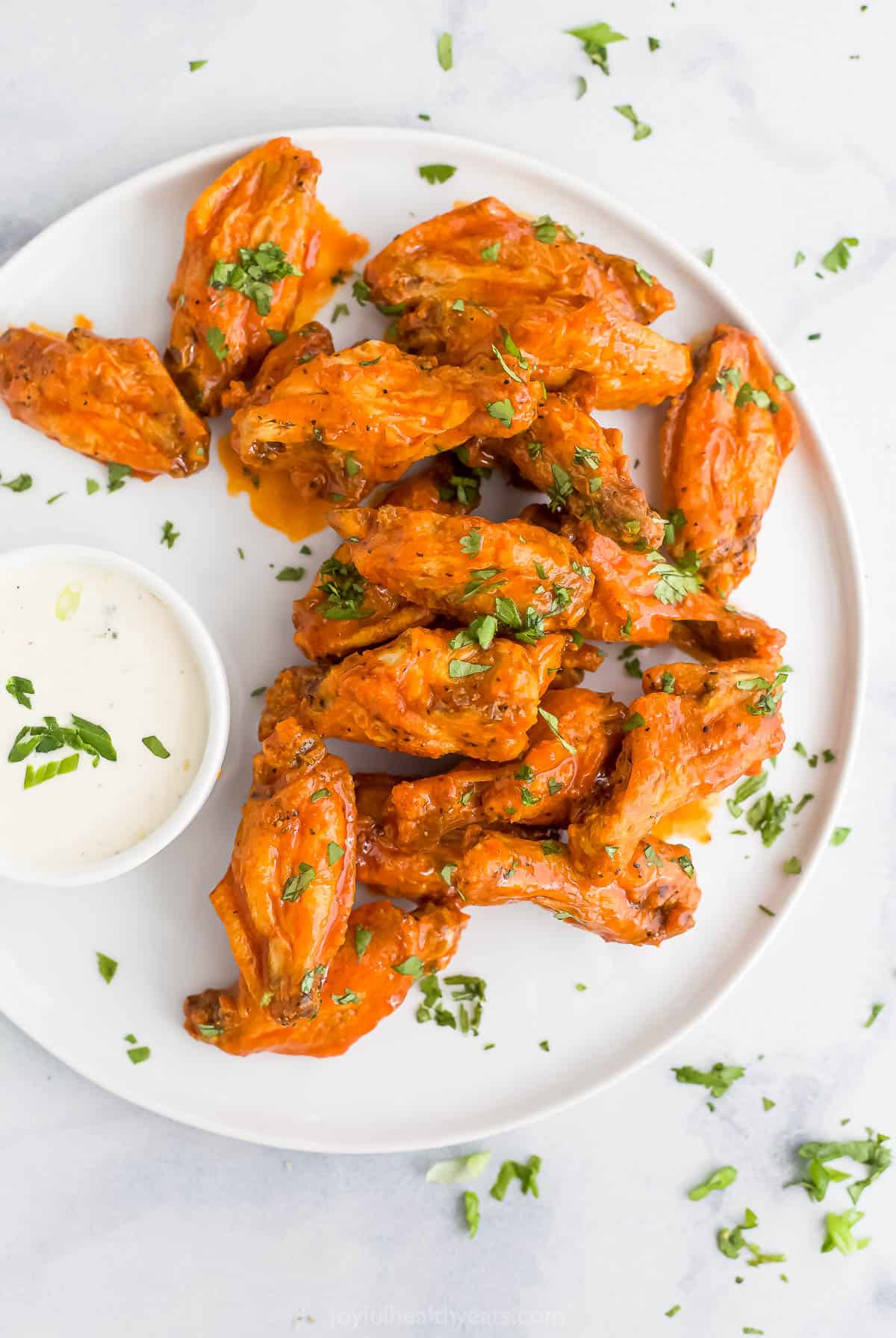 Crispy chicken wings coated in a spicy sauce on a white plate with ranch dressing