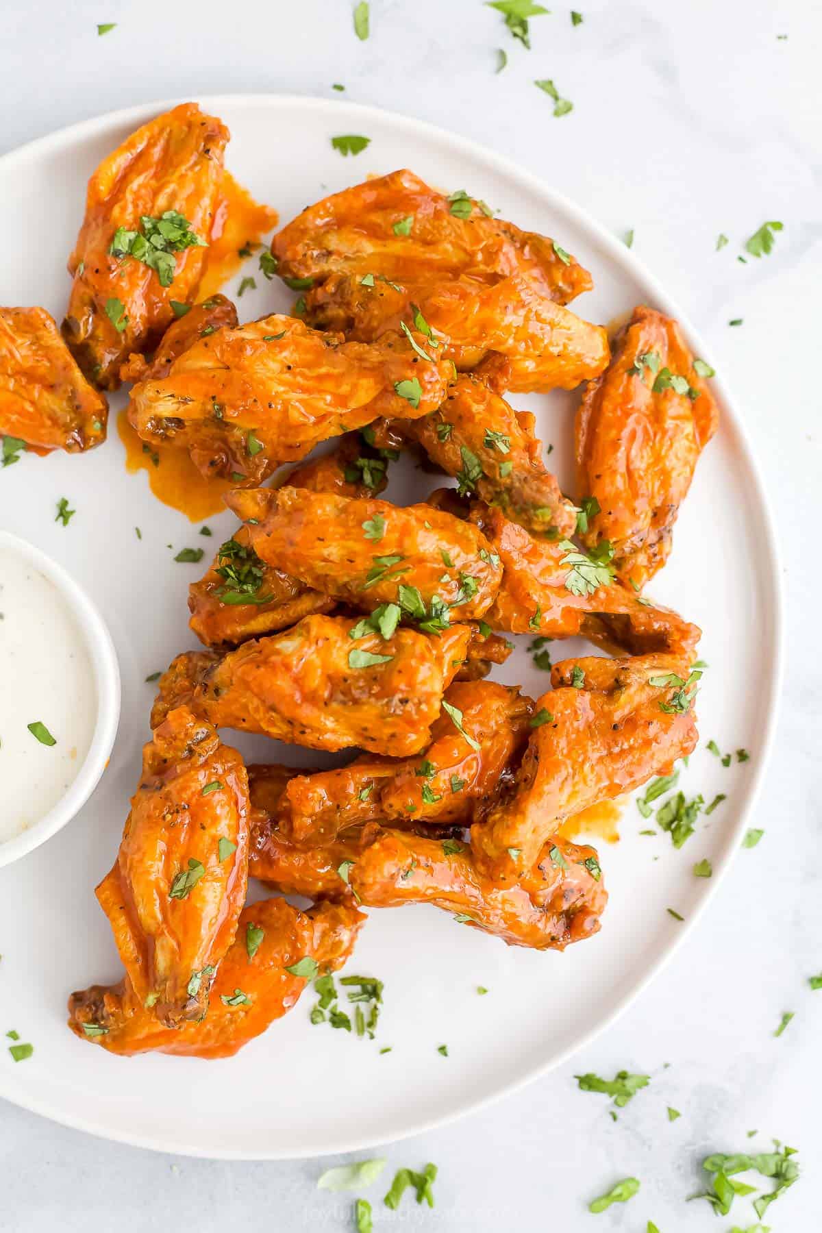 Air Fryer chicken wings covered in homemade buffalo sauce with chopped herbs as a garnish