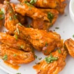 A close-up shot of chicken wings on a plate garnished with finely chopped parsley