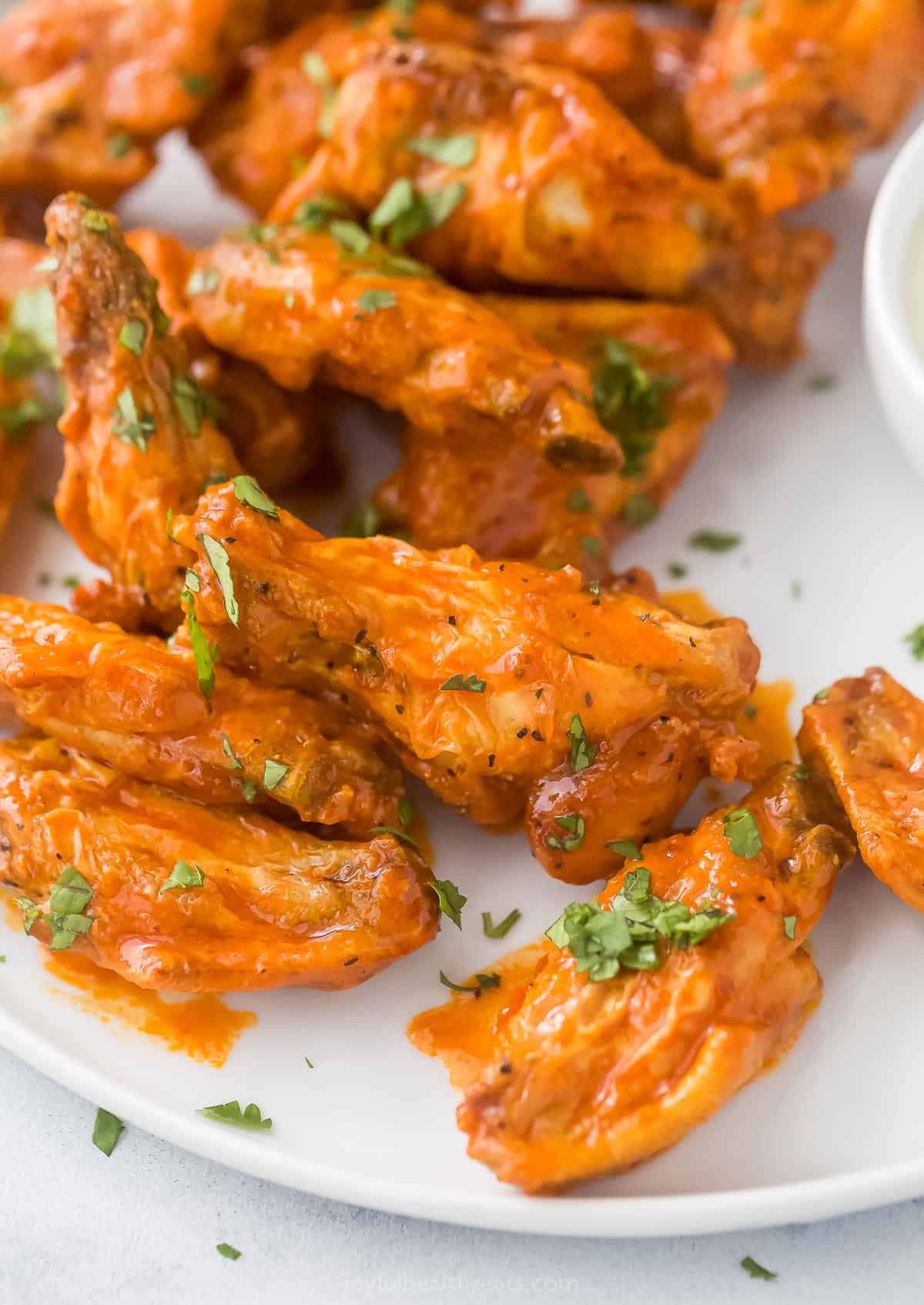 A close-up shot of chicken wings on a plate garnished with finely chopped parsley