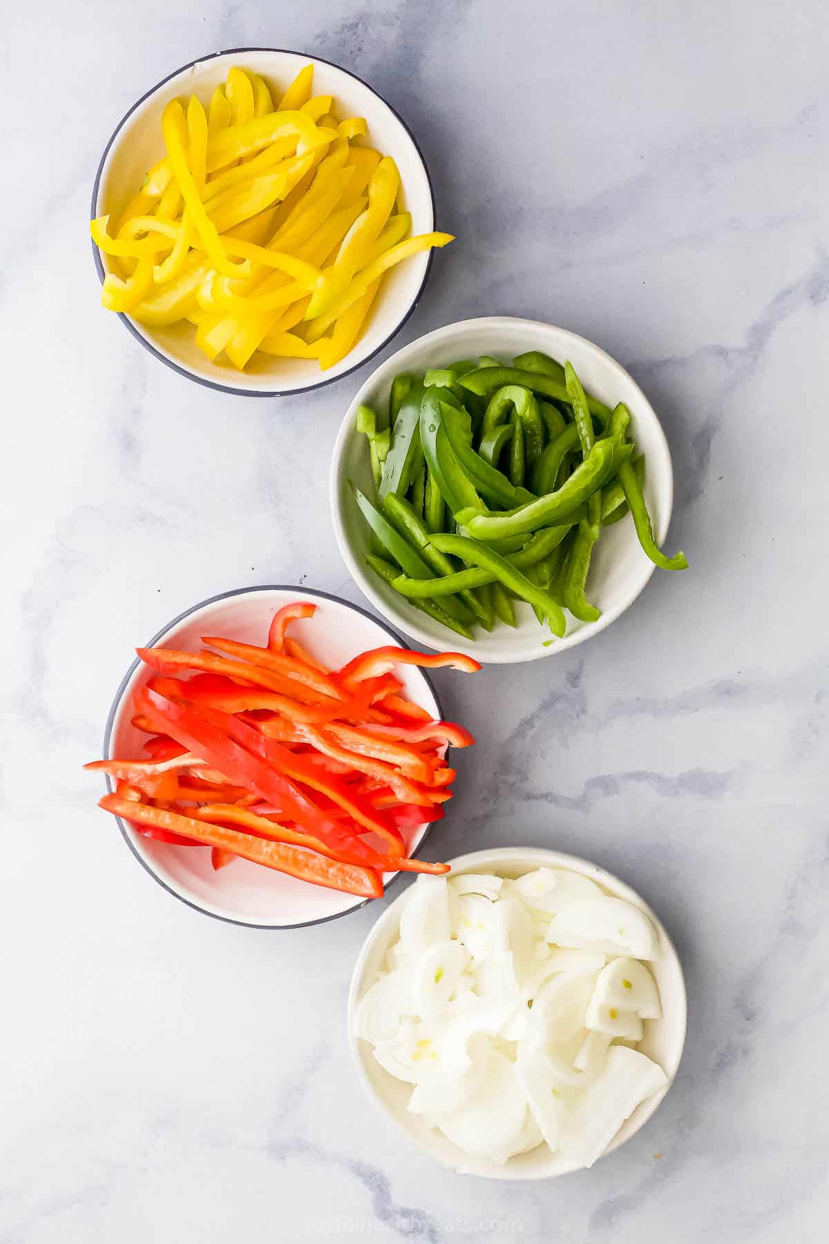Yellow, green, and red bell peppers and yellow onion sliced in bowls