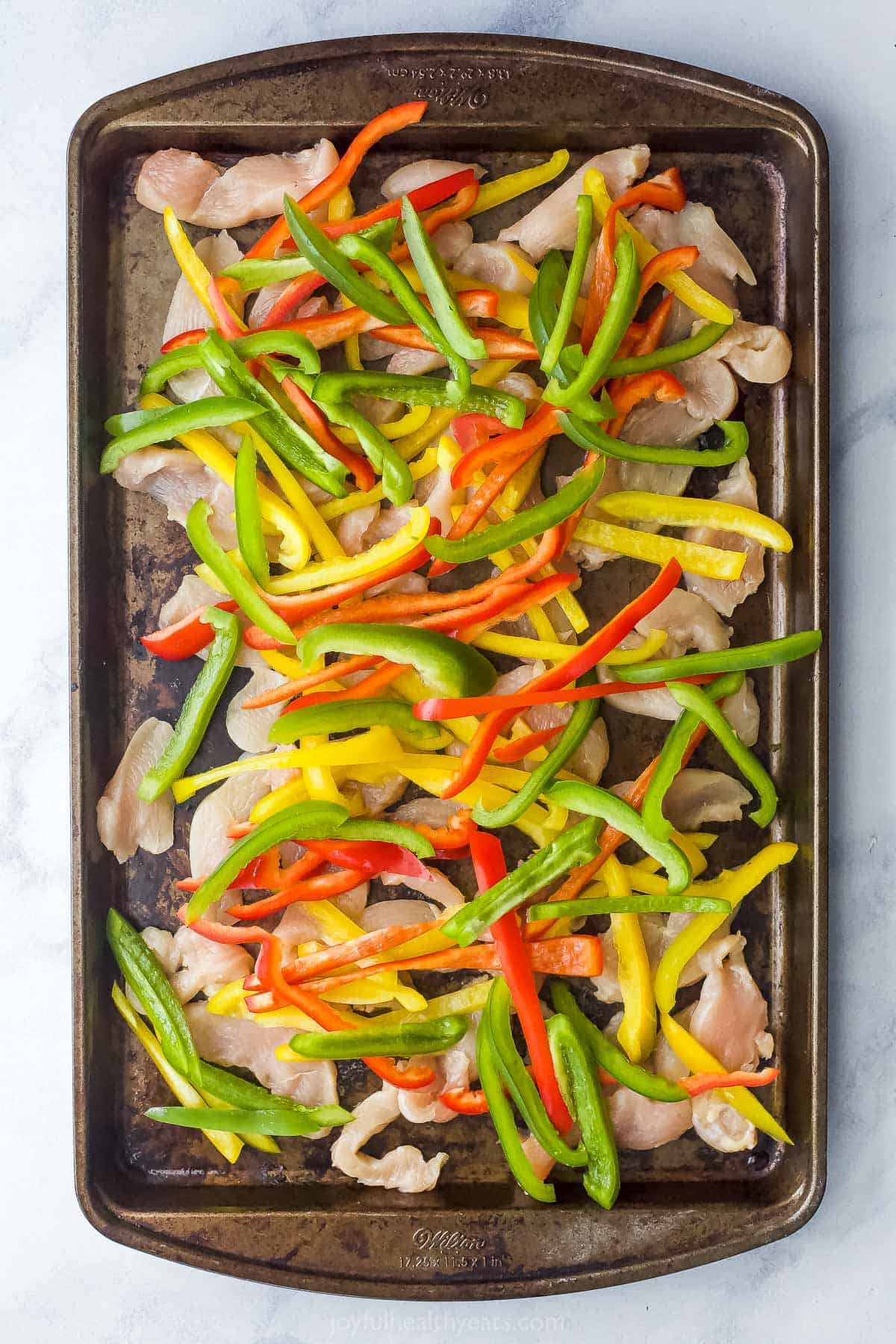 Bell peppers over top of slices of chicken breast on a sheet pan
