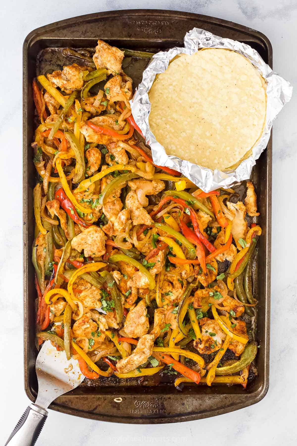 Overhead view of sheet pan chicken fajitas with tortillas on the side