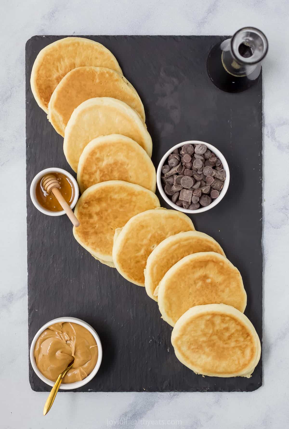 Pancakes, chocolate chips, honey, peanut butter and maple syrup on top of a large black platter