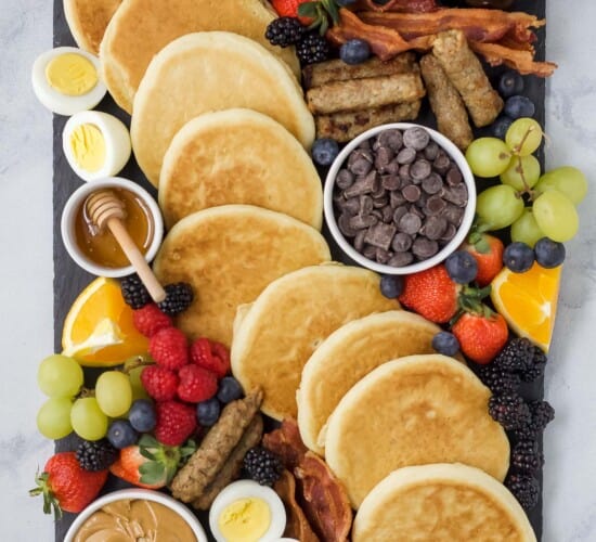 A charcuterie board containing a bunch of breakfast food including pancakes and maple syrup