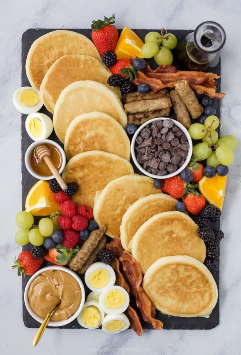 A charcuterie board containing a bunch of breakfast food including pancakes and maple syrup