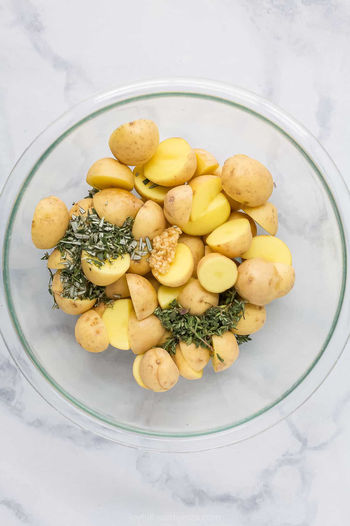 Halved baby potatoes in a bowl with fresh herbs