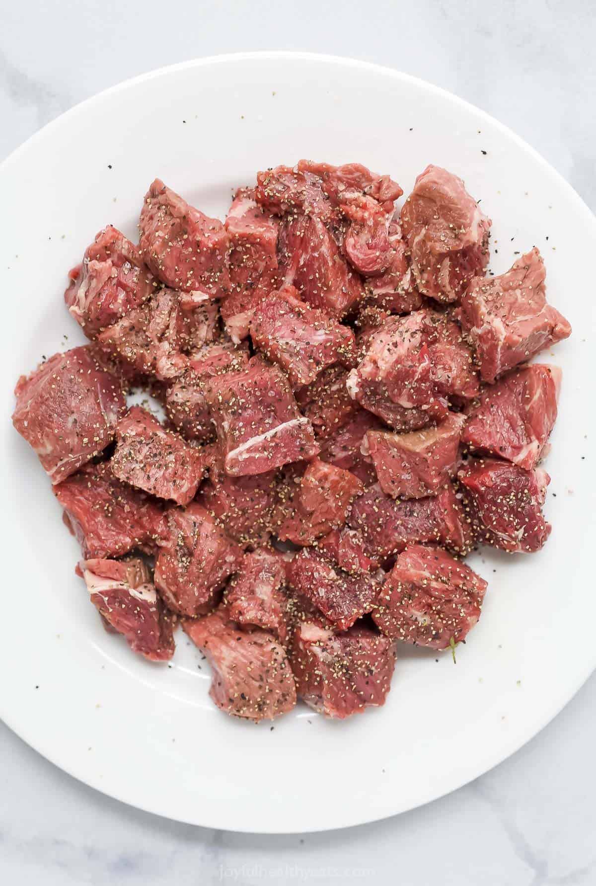 Cubes of sirloin steak seasoned with salt and pepper on a white plate